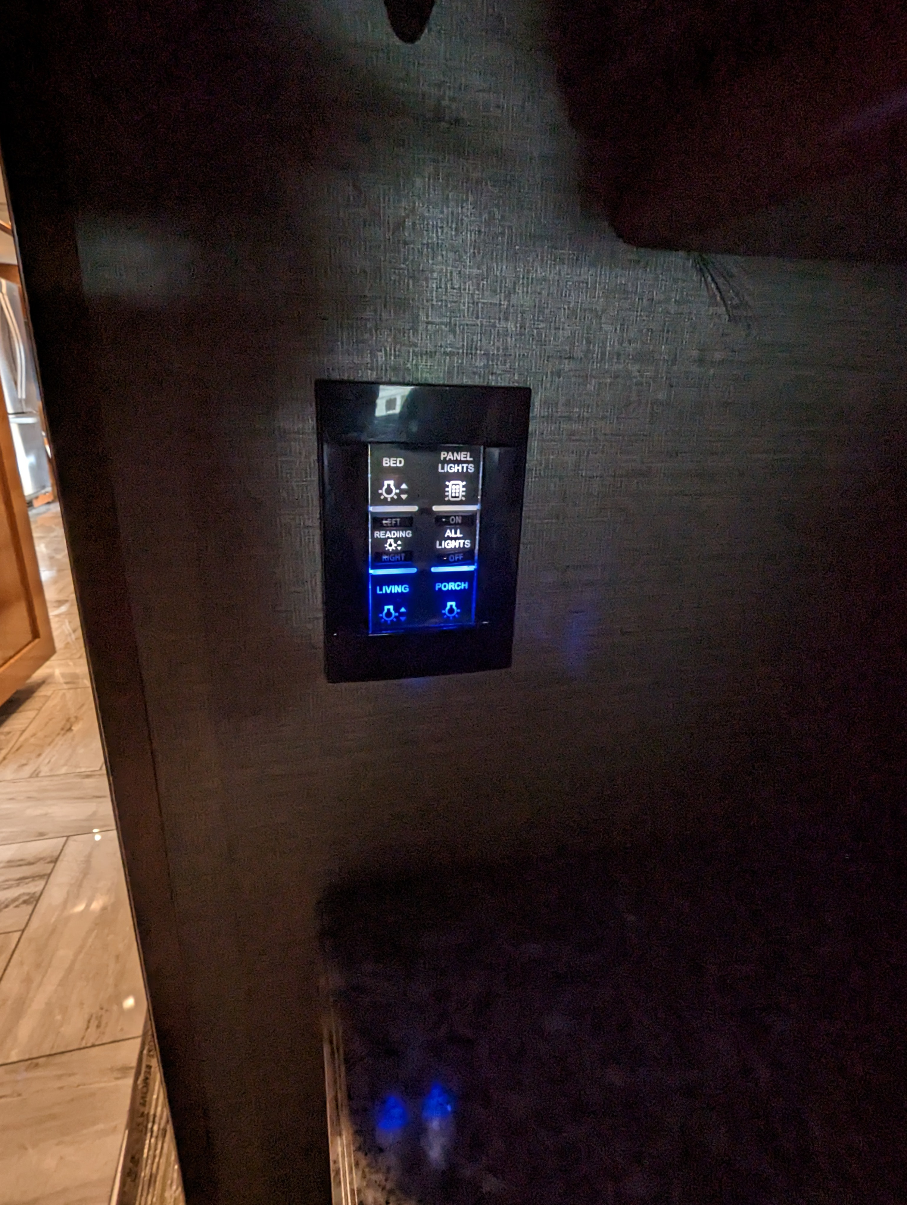 Modern RV rental light panel, glowing blue. Controls for bed, reading, living, and exterior porch lights are visible on a dark wall.. Fleetwood Discovery 2017