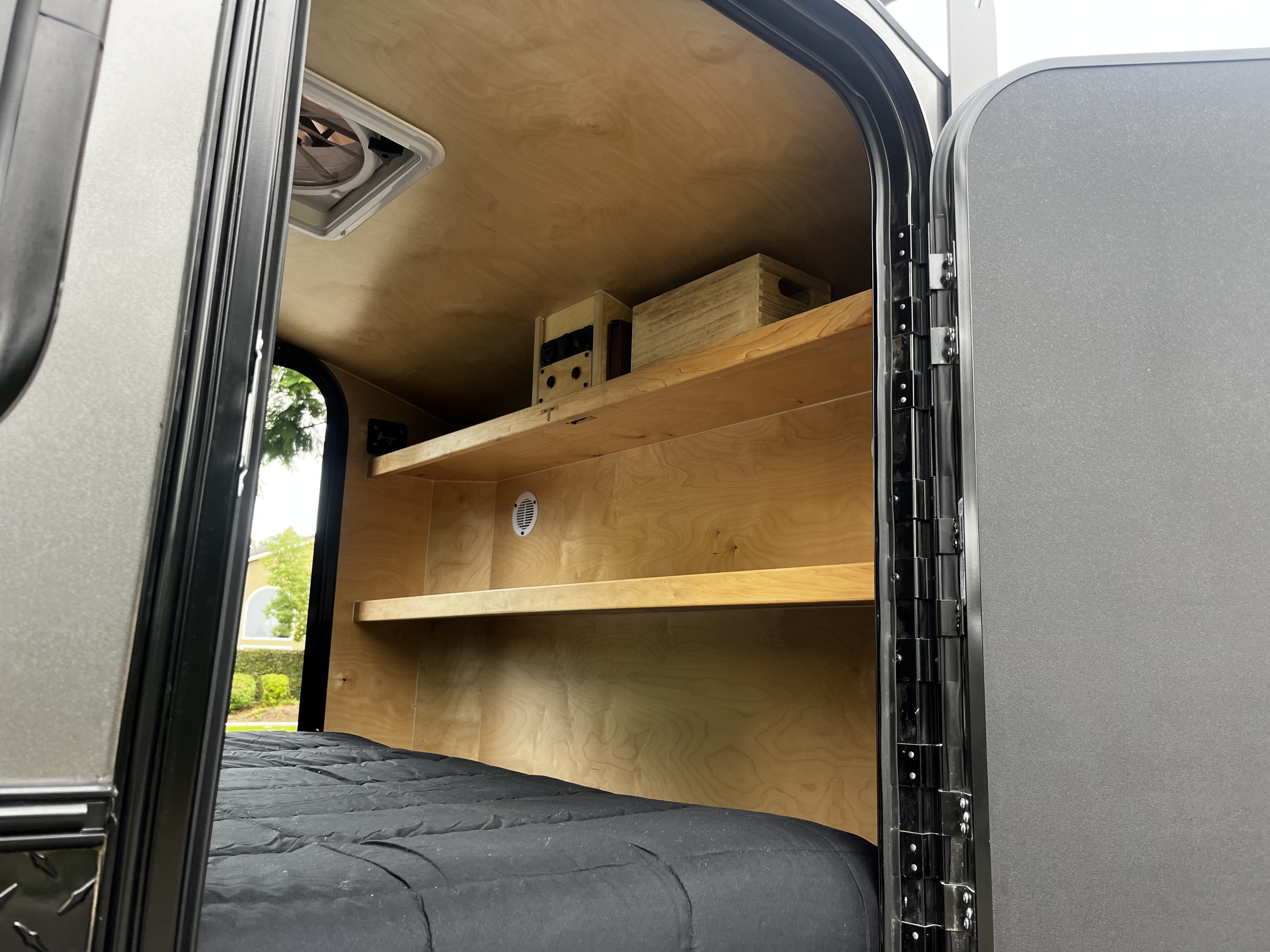 Teardrop RV rental interior: cozy wooden walls, built-in shelves with controls, a comfy bed, and an open door.. Hiker MXL5x10 2022