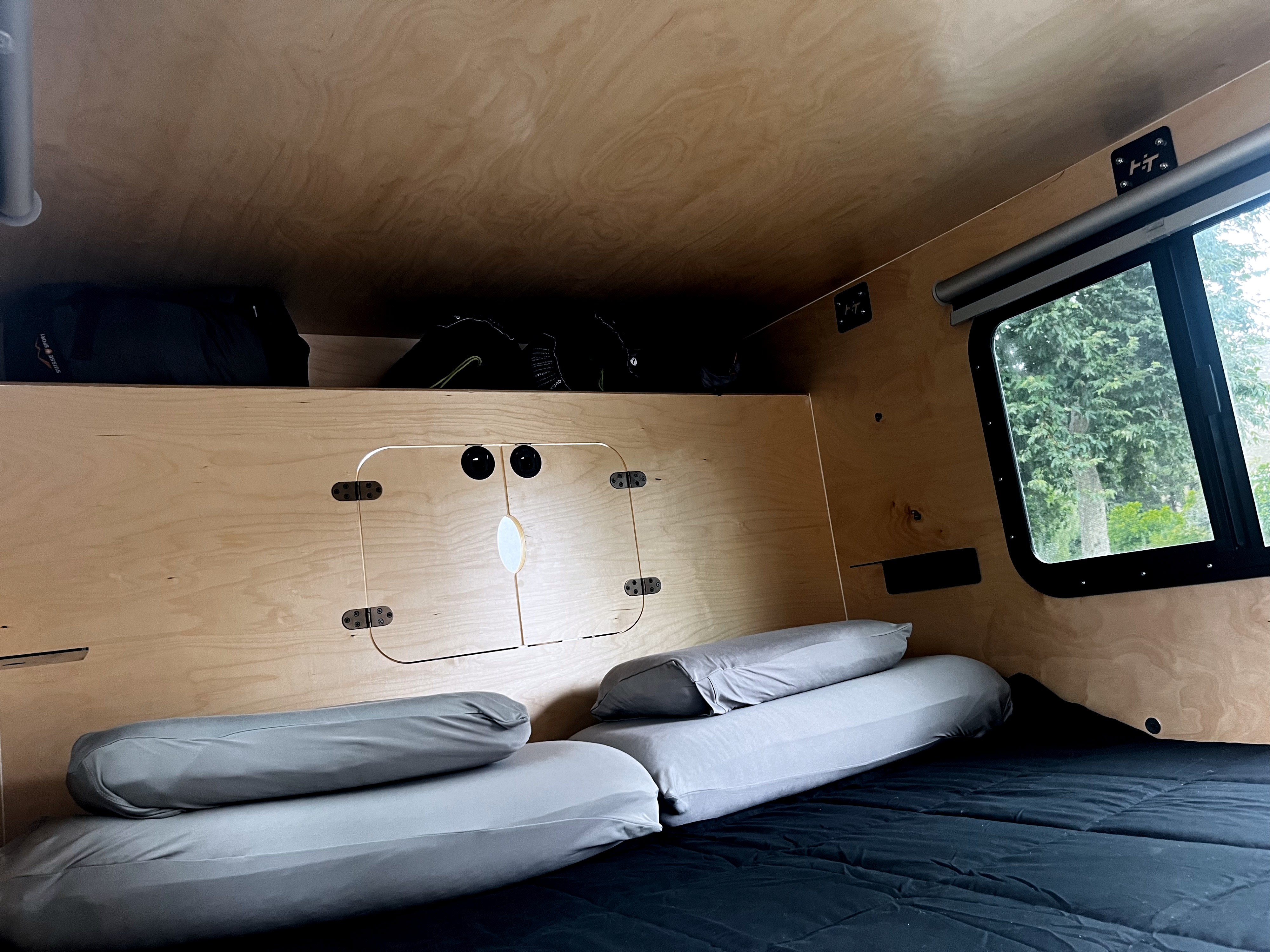 Cozy RV rental interior with wood walls, comfortable bed, overhead storage, and a window offering a lush green view outside.. Hiker MXL5x10 2022