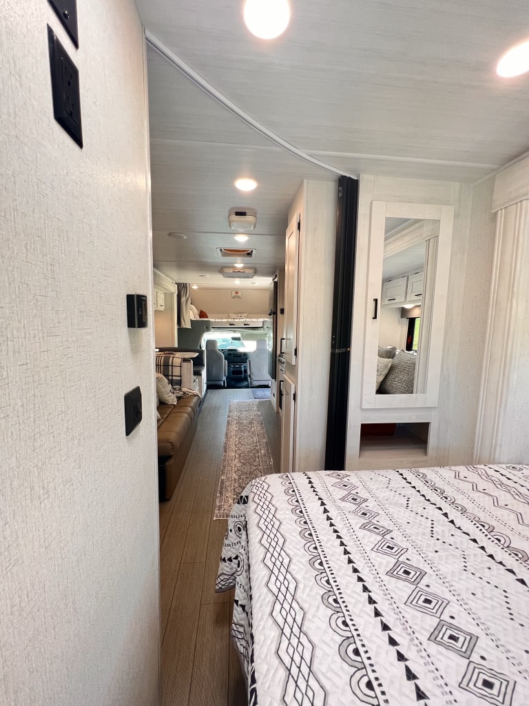 Explore this bright rv rental interior: A long hallway leads past a cozy bed to the living & driver's cab.. East to West Entrada 2022