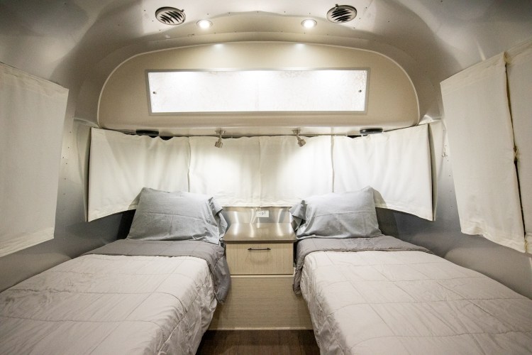 Cozy Airstream rv rental interior featuring twin beds, a nightstand, and overhead lighting for comfortable travel.. Airstream International 2020