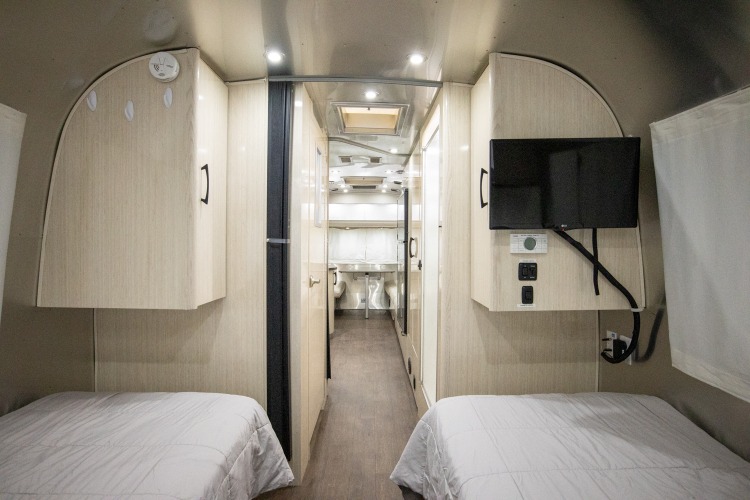 Inside this cozy RV rental: twin beds with storage, and a hallway leading to the compact kitchen/bath area. Ideal for travel.. Airstream International 2020