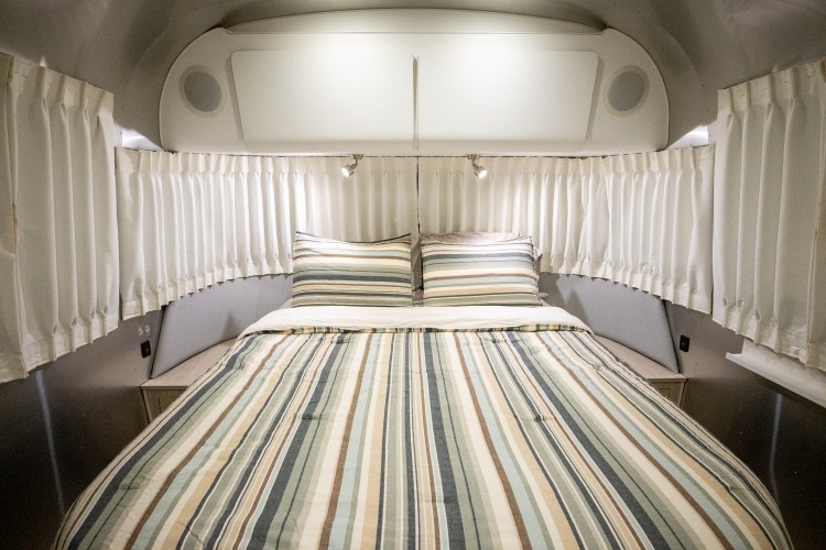 Cozy RV rental bedroom with striped bedding, reading lights, and white curtains along the curved walls.. Airstream Globetrotter 2019