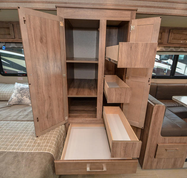 RV rental interior: central open storage unit with shelves and multiple pull-out drawers, alongside a bed and dinette area.. Entegra Coach Odyssey 2020