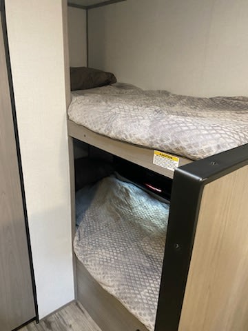 Cozy bunk beds inside an RV rental, neatly made with light grey patterned bedding. A brown pillow is on the top bunk.. Dutchmen Coleman Lantern LT 2023