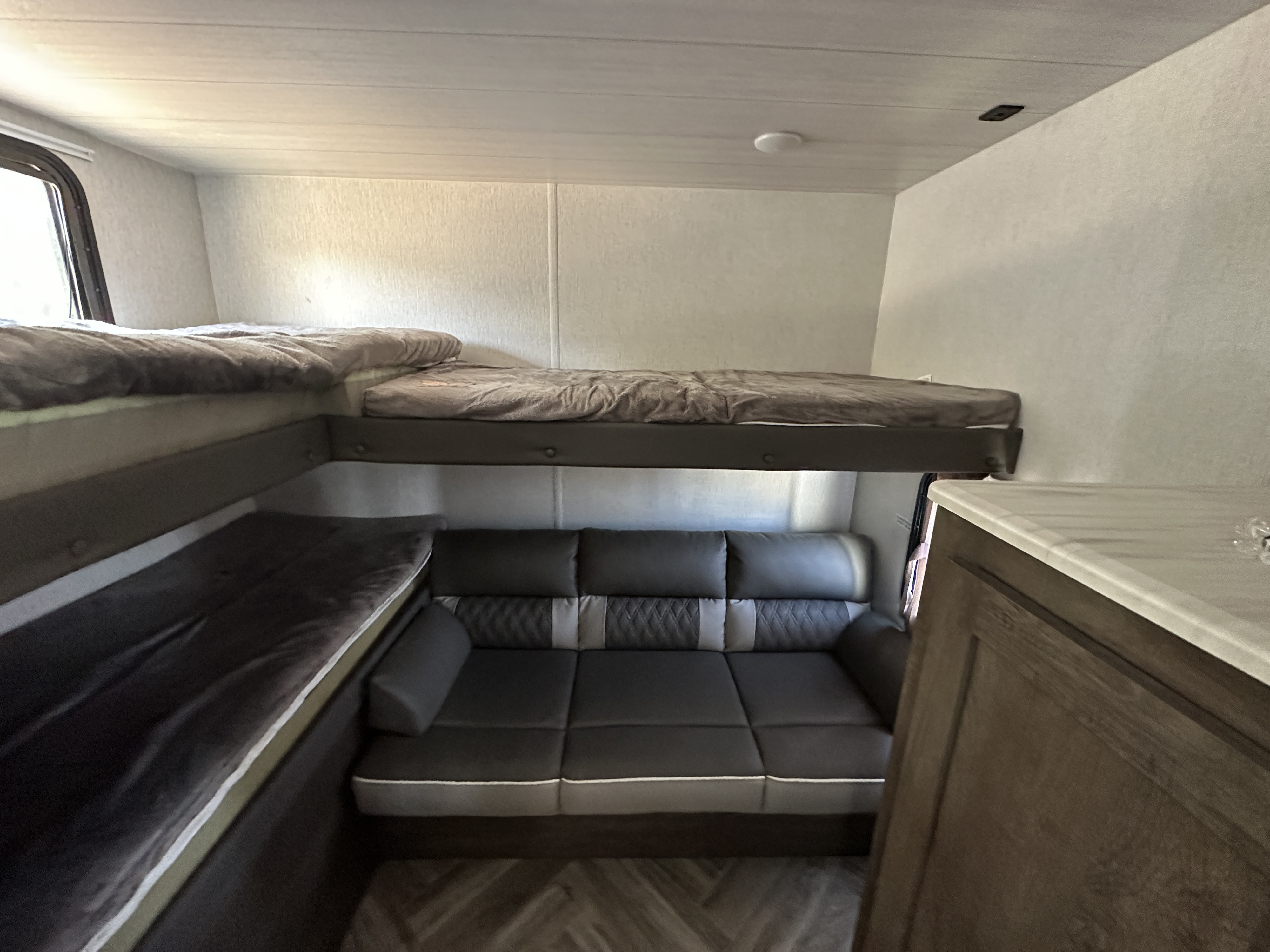 RV rental interior features bunk beds above a sofa, with light walls and a patterned floor, offering a compact living space.. Forest River Wildwood X-Lite 2022