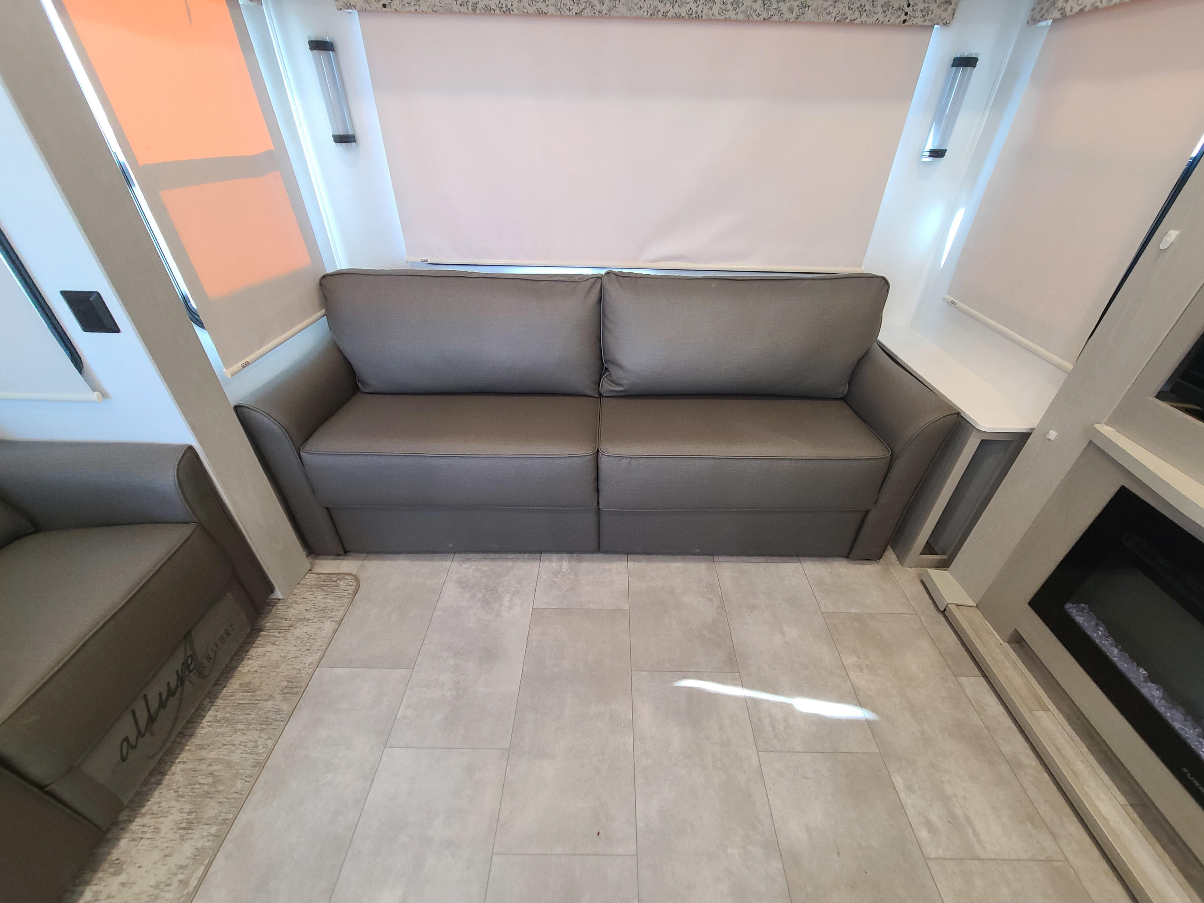 Cozy RV rental interior featuring a gray sofa, window shades, and a fireplace unit with tiled flooring.. Palomino Columbus 2022