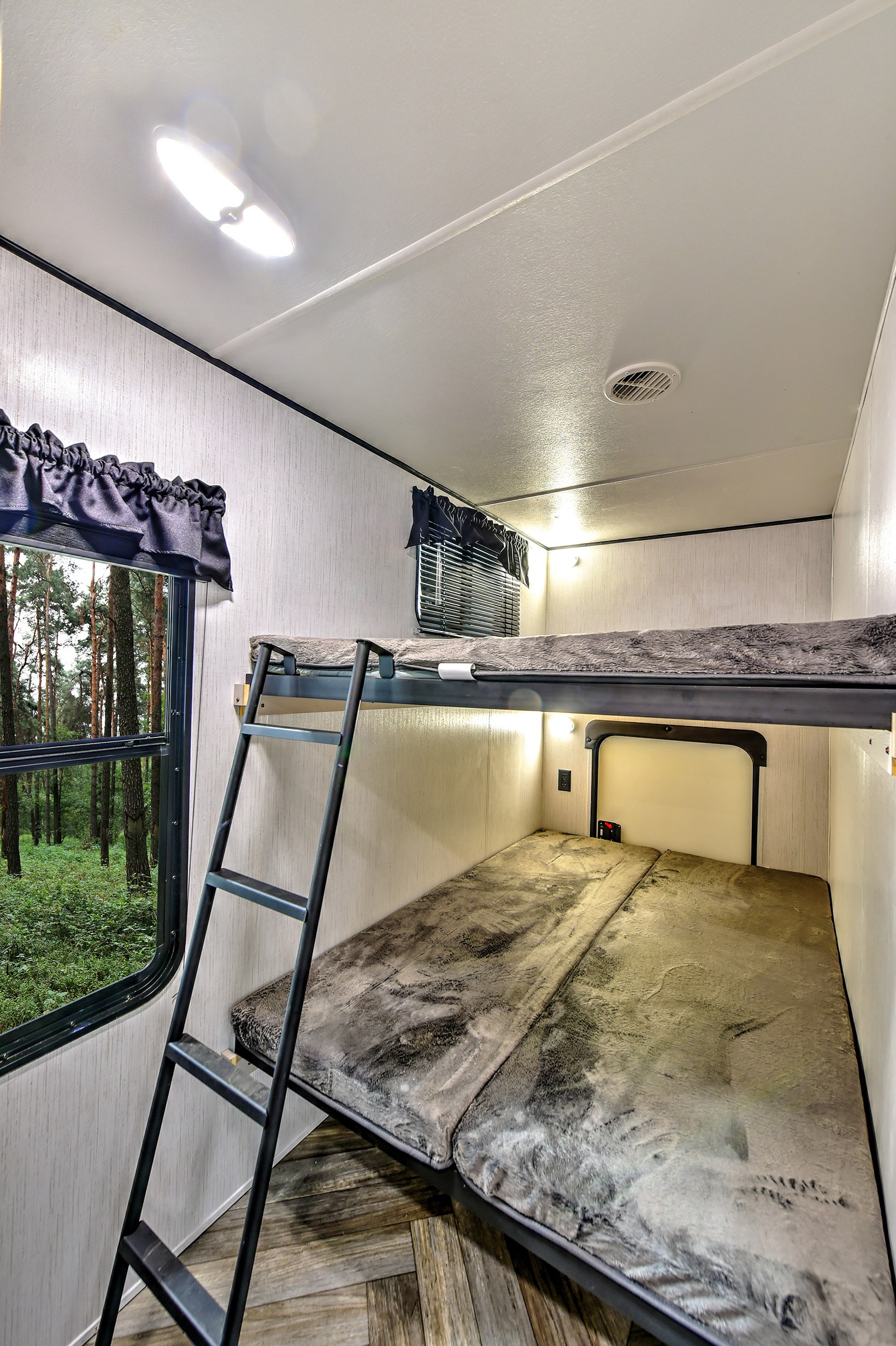 Spacious RV rental interior featuring cozy bunk beds with a ladder and a scenic window view of a lush forest.. Heartland RVs Prowler 2021