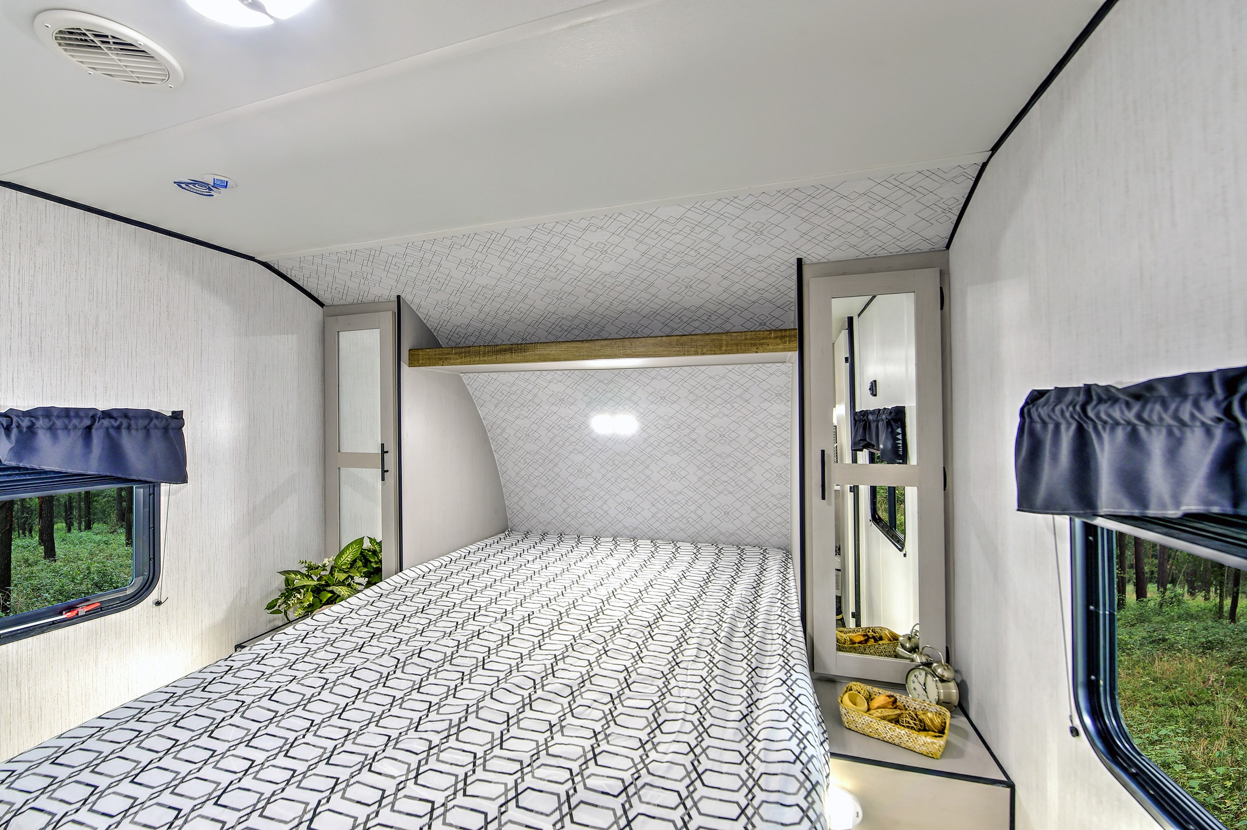 Comfortable RV rental bedroom with a geometric patterned bed, convenient storage, and serene forest views for your next adventure.. Heartland RVs Prowler 2021