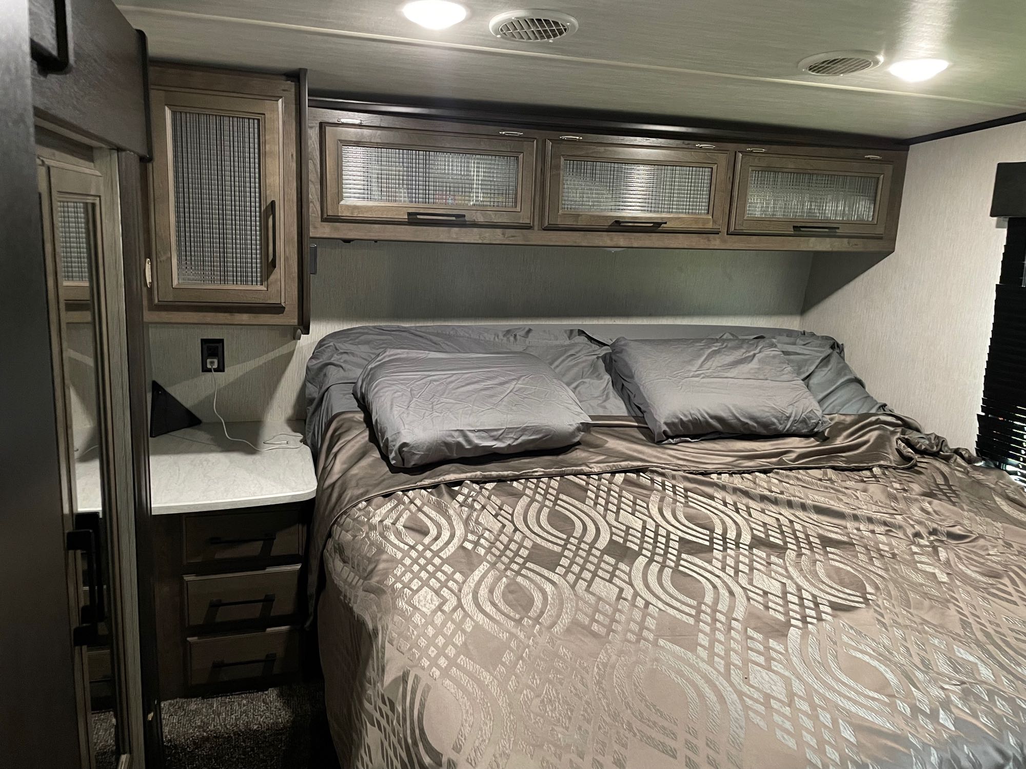 Cozy RV rental bedroom featuring a comfortable bed with patterned bedding, overhead storage, and a nightstand.. Heartland Torque 2019