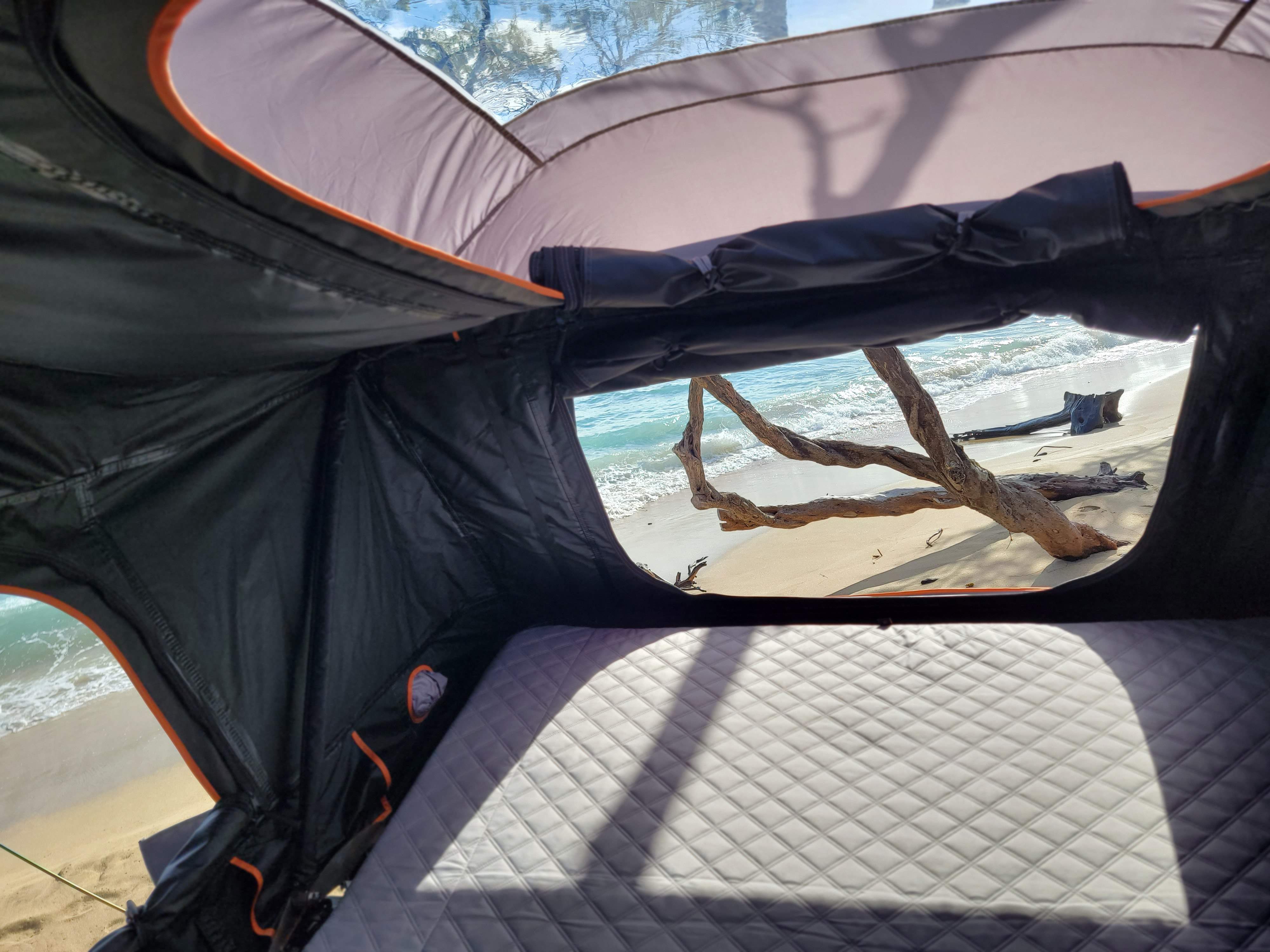 RV rental adventure: Enjoy a serene beach view from inside a comfortable rooftop tent with a quilted mattress.. Subaru Ascent 2023