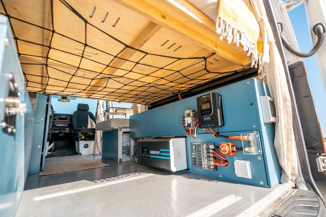 RV rental interior featuring a Renogy power system, overhead bed, and cargo net storage in a camper van.. Mercedes-Benz Sprinter 2019