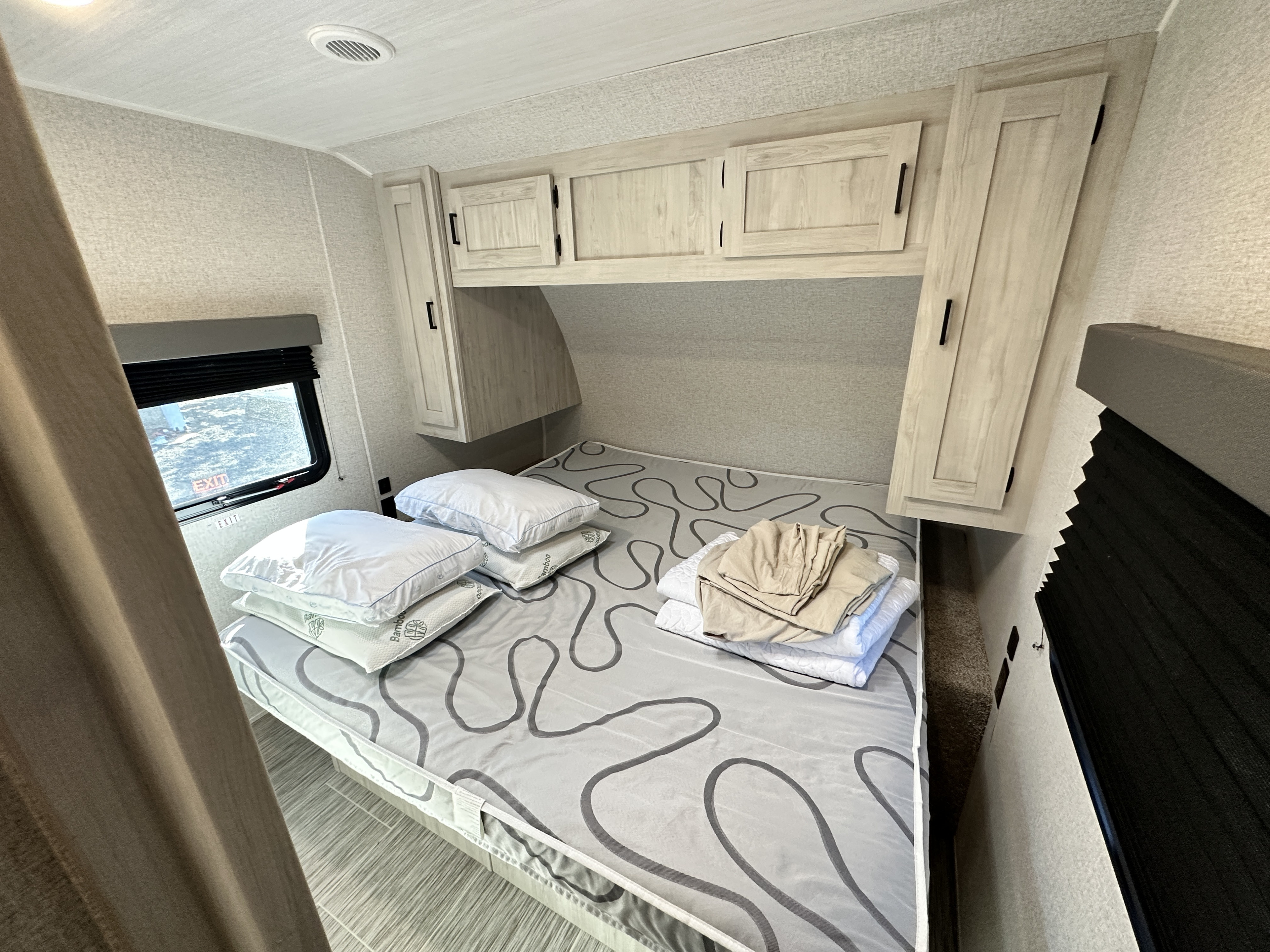 Cozy RV rental bedroom featuring a bed, pillows, linens, overhead storage, and a window.. Forest River Silver Lake 2023