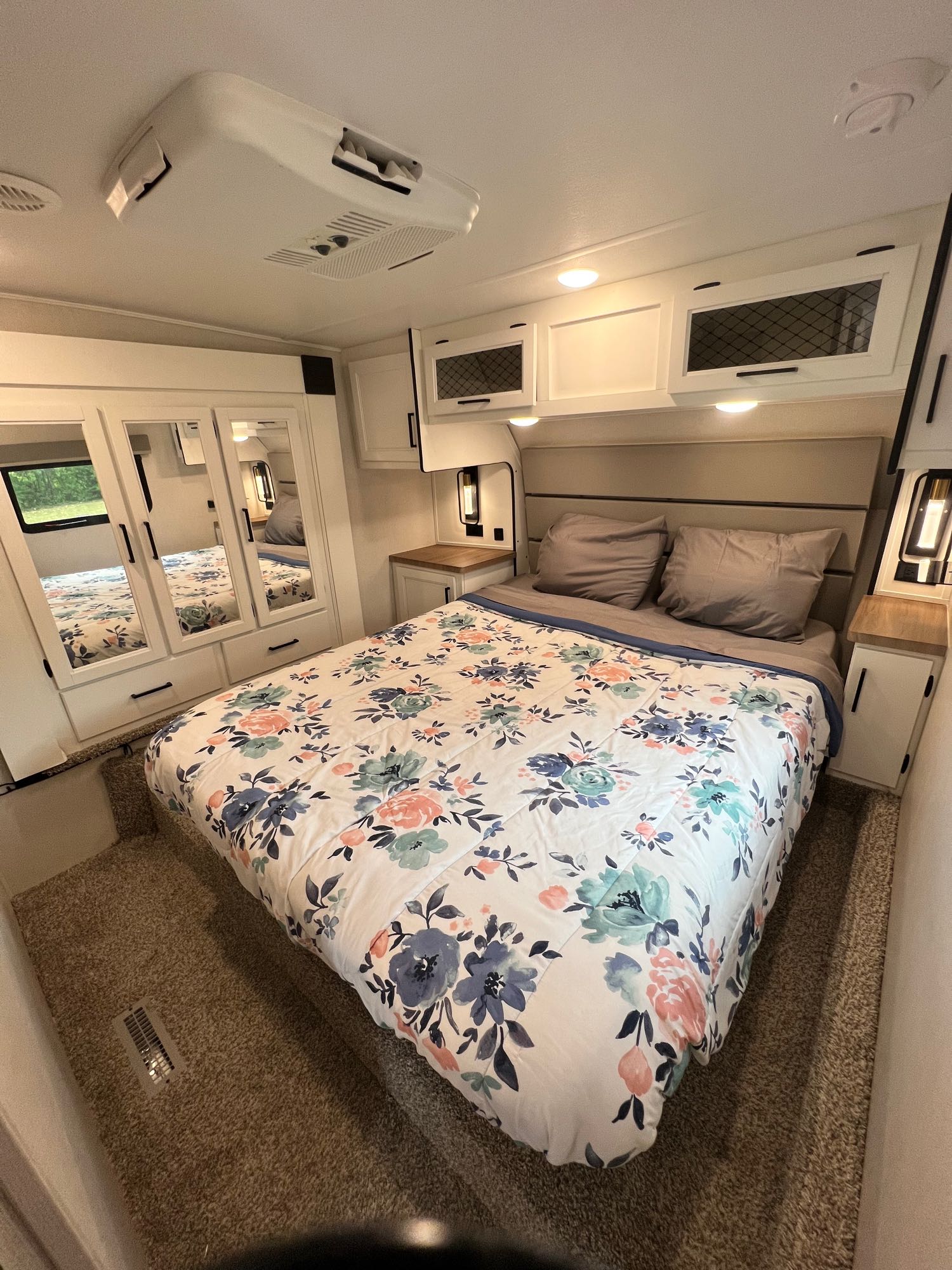 Cozy RV rental bedroom featuring a floral bed, built-in storage, and mirrored closet doors.. Crusader Lite 2022