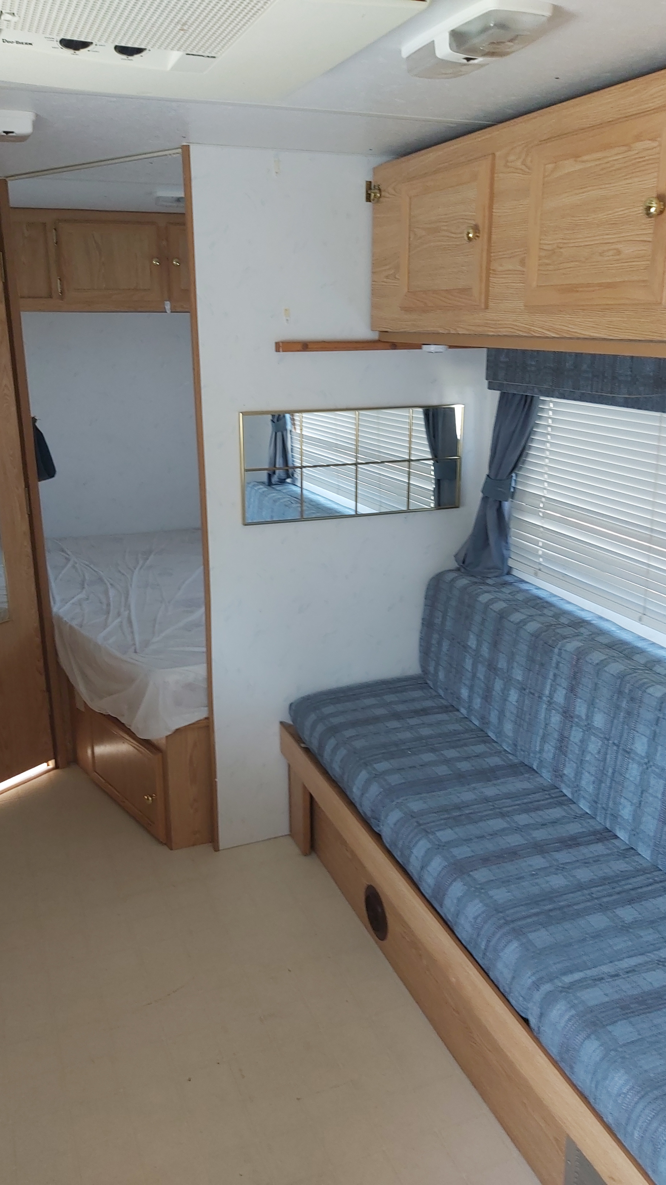 Tour this RV rental interior: cozy bedroom with bed & living area featuring blue plaid bench, overhead cabinets, and window.. Kustom Koach Pt230 1998