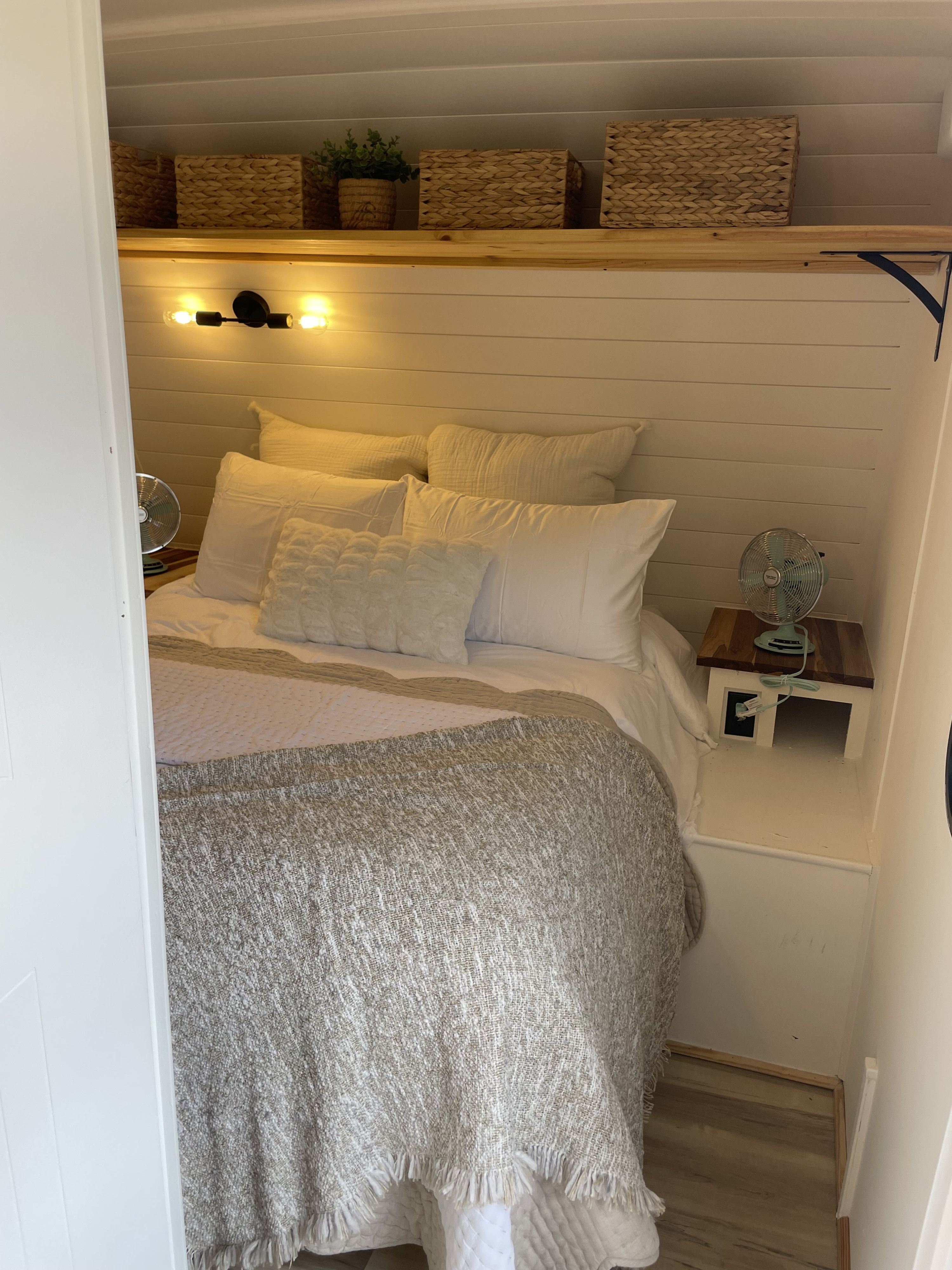 Cozy RV rental bedroom with white bed, shiplap walls, wooden shelf, warm lighting, and retro fans.. Heartland RVs Mallard 2016
