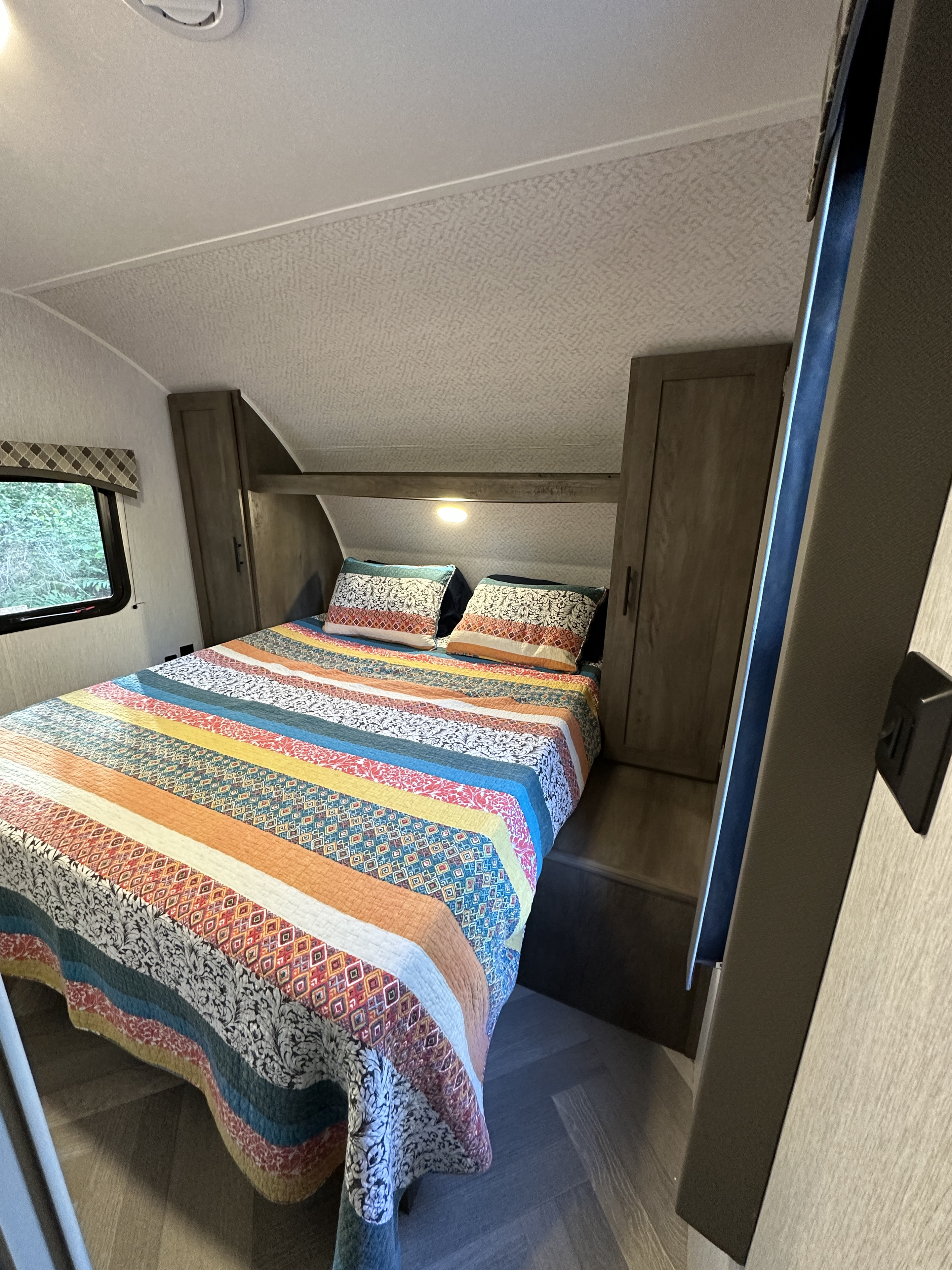 Cozy RV rental bedroom with colorful patterned bed, built-in storage, and a window showing foliage.. Forest River EVO Lite 2400BH 2022