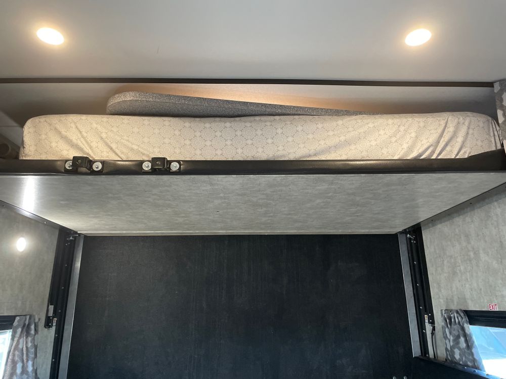 Inside an RV rental, showing a high bunk bed with a mattress and an open lower garage space below. Features recessed lighting.. Eclipse Recreational Vehicles Attitude 2018