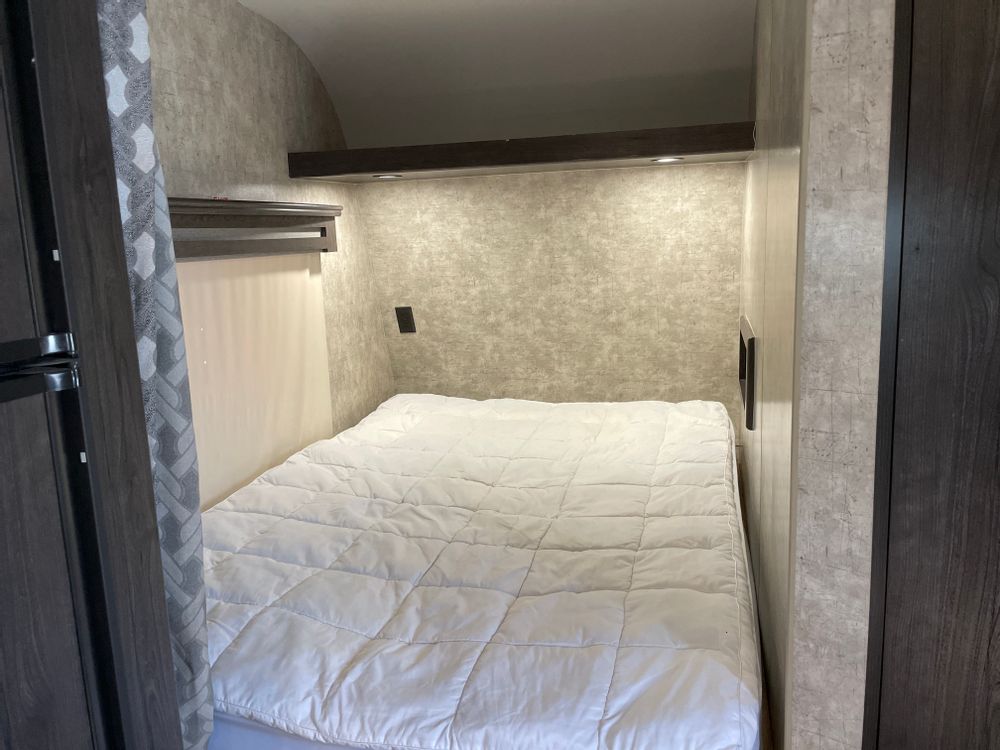 An RV rental's cozy bedroom features a comfortable bed, textured walls, and practical shelving with ambient lights.. Eclipse Recreational Vehicles Attitude 2018