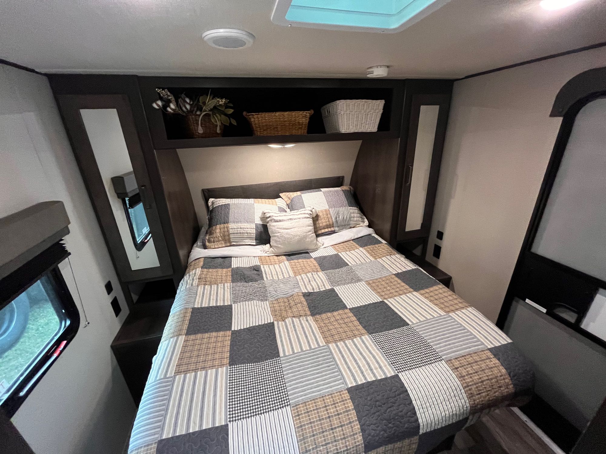 Cozy RV bedroom interior features a patchwork quilt bed, built-in storage, and window, ideal for an RV rental.. Grand Design Transcend Xplor 2022