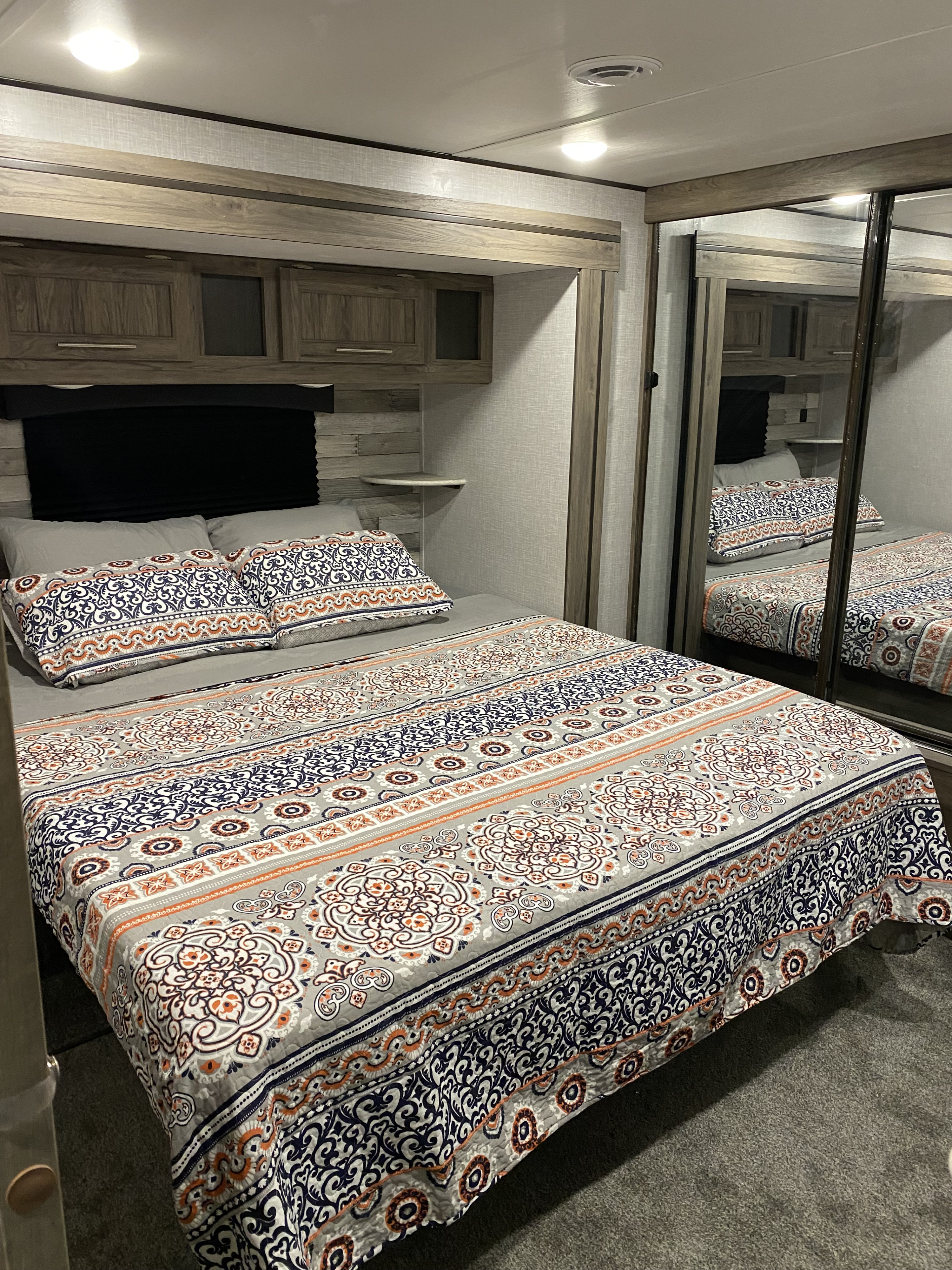 An inviting RV rental bedroom with a decorative bedspread, practical overhead storage, and mirrored closet.. Crossroads RV Zinger 2022