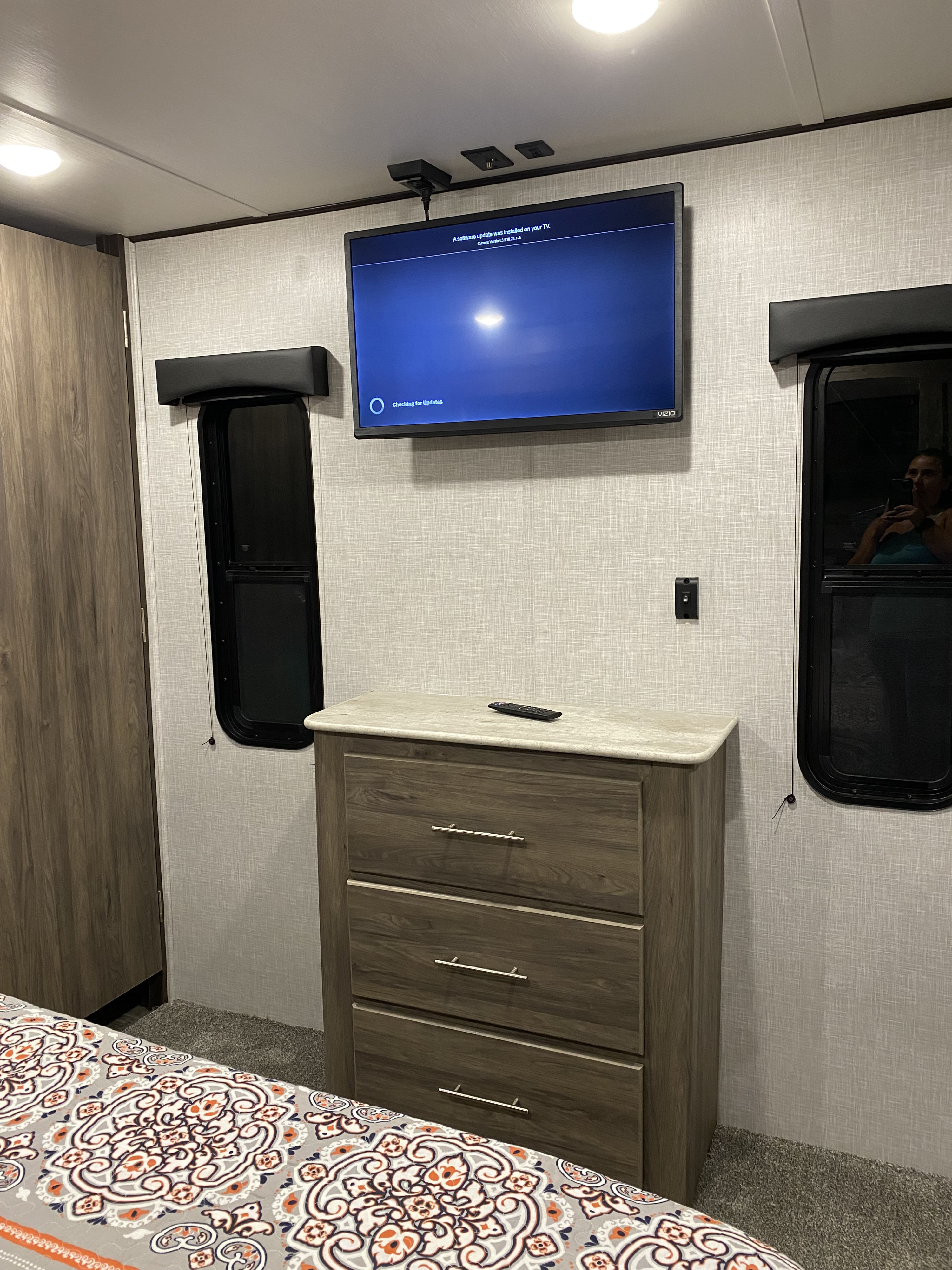 Cozy RV rental bedroom featuring a mounted Vizio TV updating, a dresser, and two windows with shades.. Crossroads RV Zinger 2022
