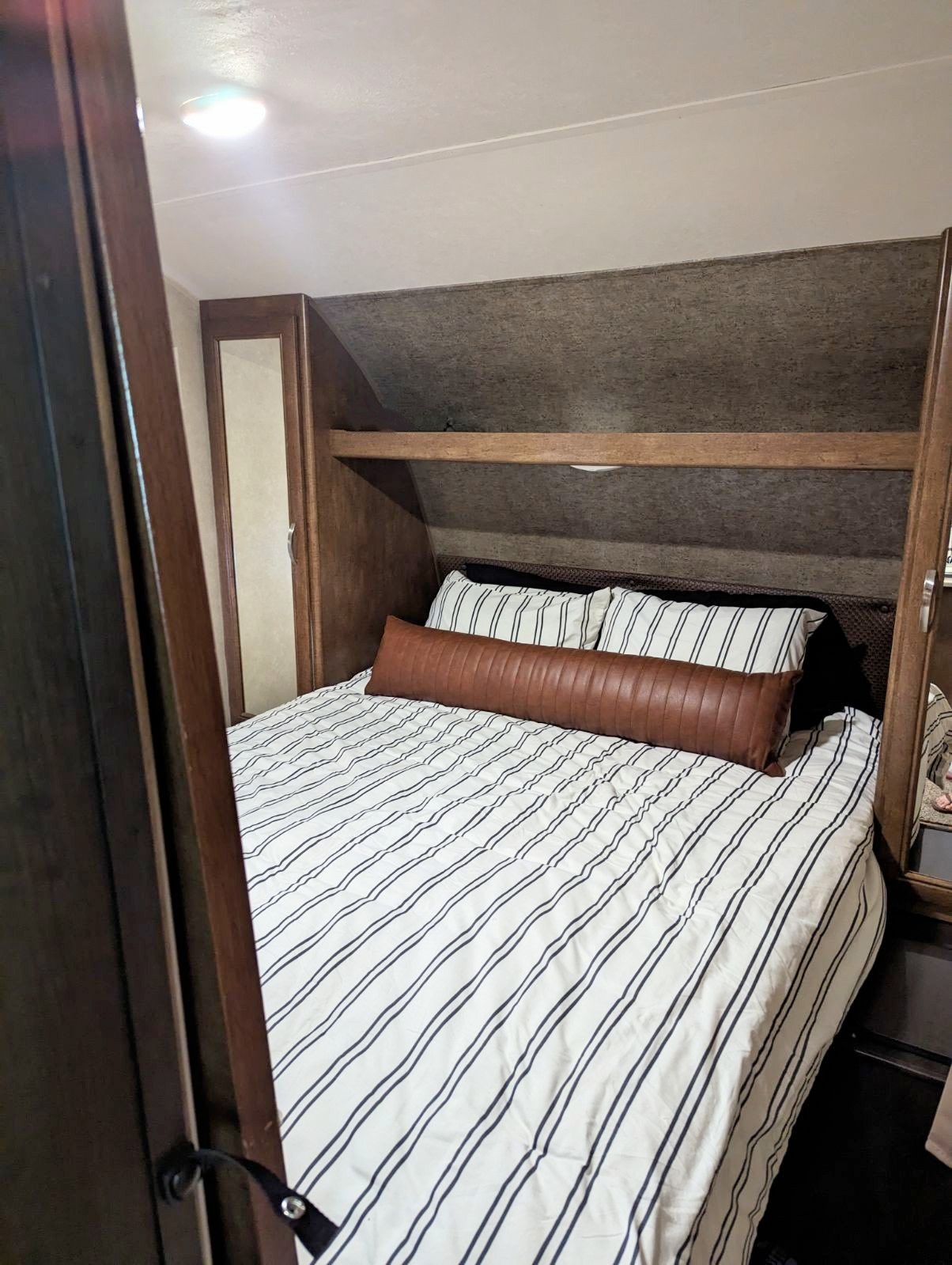 Cozy RV rental bedroom featuring striped bedding, a brown bolster pillow, and built-in wooden storage.. Forest River Salem 2017