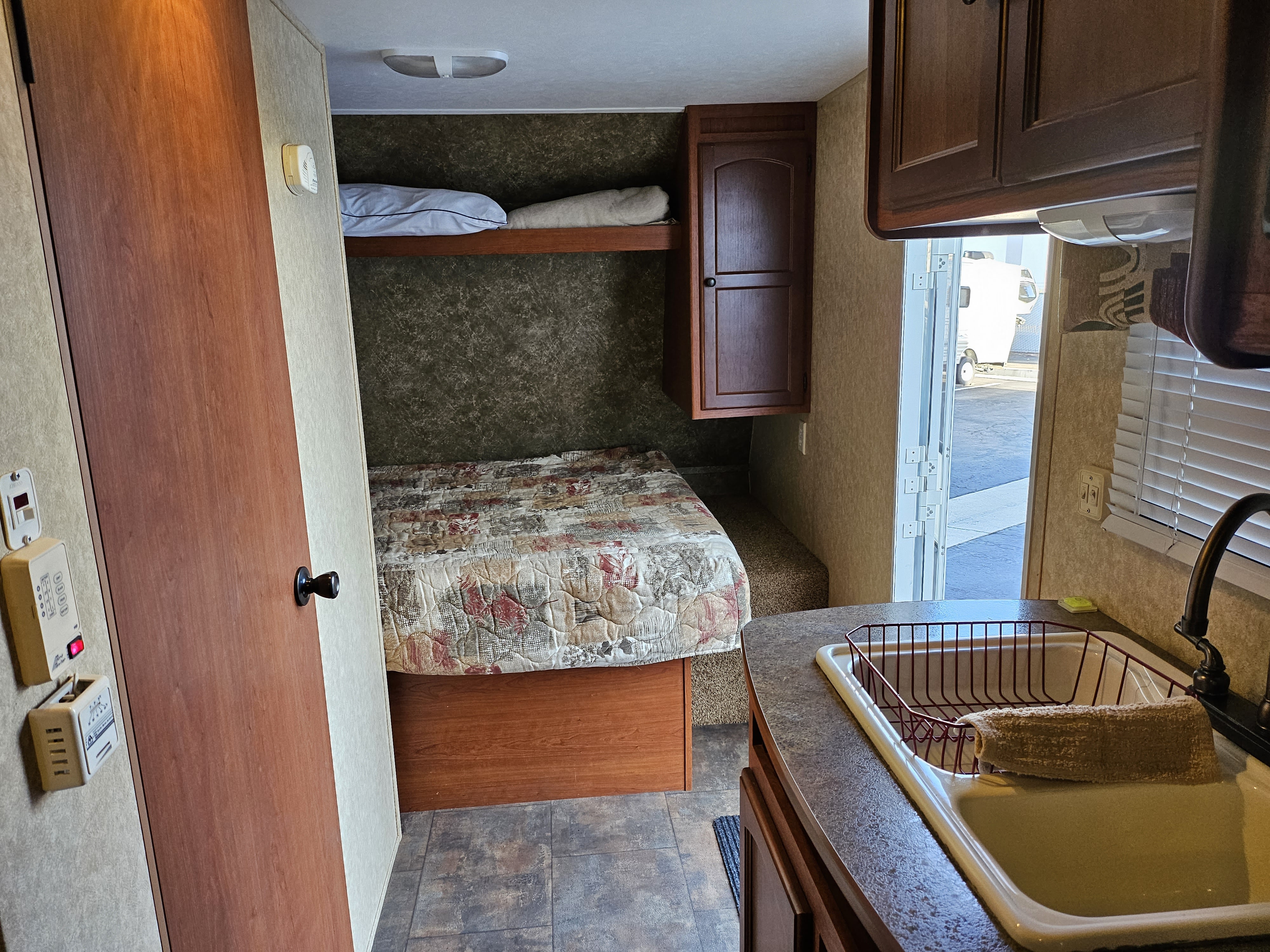 Step into this RV rental's inviting interior: features a bed, upper bunk, compact kitchen with sink, and an open exit.. Dutchmen Sport SS 2011