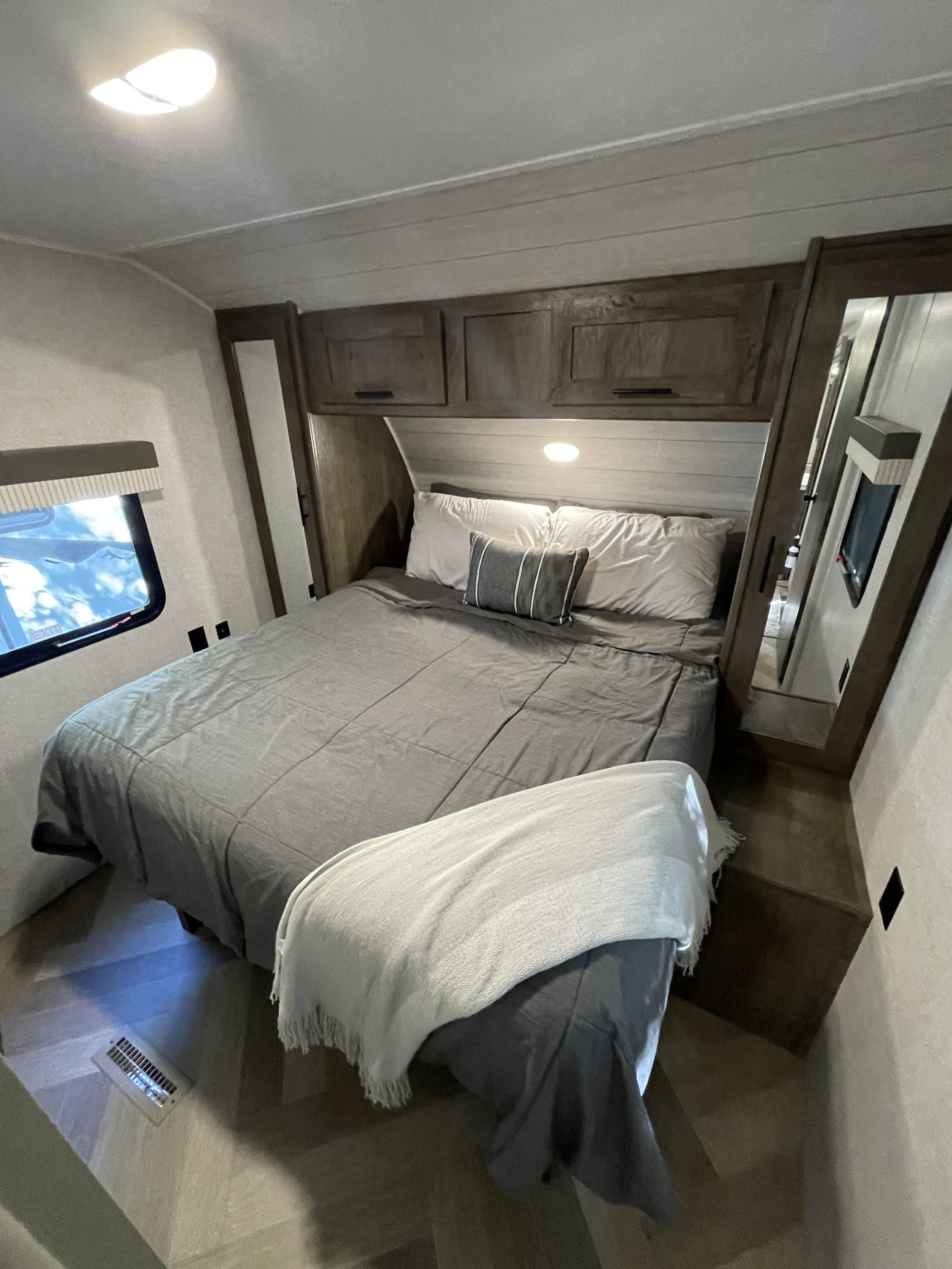 Step into comfort! This RV rental bedroom features a cozy bed with grey bedding, overhead cabinets, and a window for scenic views.. Forest River Salem 2021
