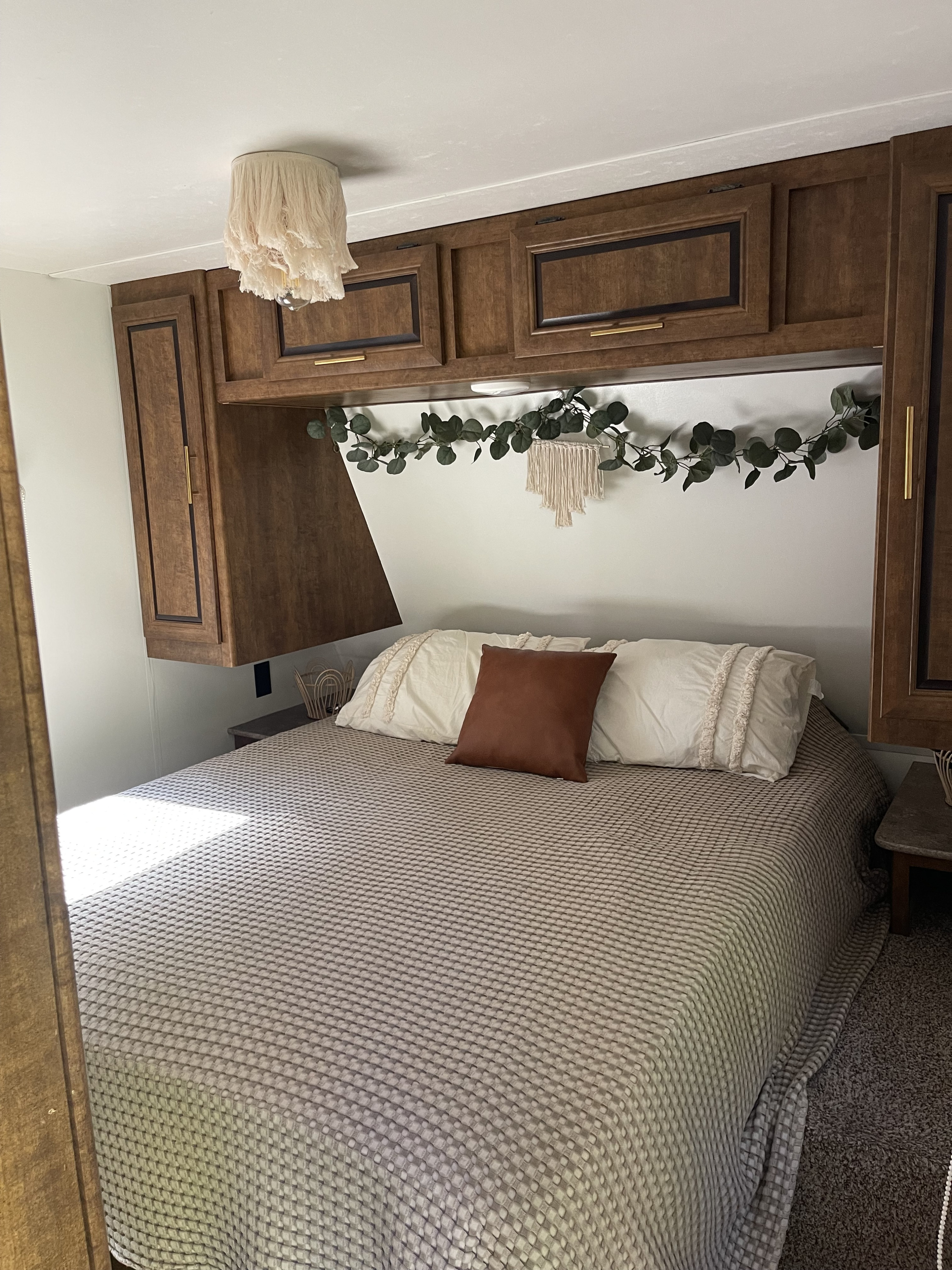 Cozy RV rental bedroom featuring a patterned bed, dark wood storage cabinets, and boho decor.. Crossroads RV Zinger 2017