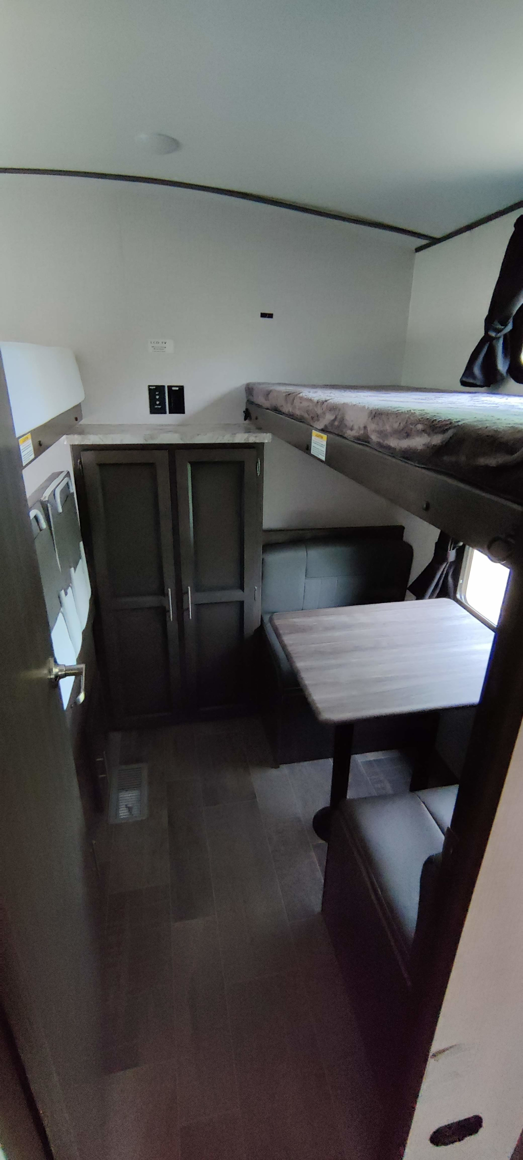 Inside this RV rental, a cozy bunk bed sits above a dinette with bench seats and a table. Storage cabinets nearby.. Crossroads RV Sunset Trail Super Lite 2021