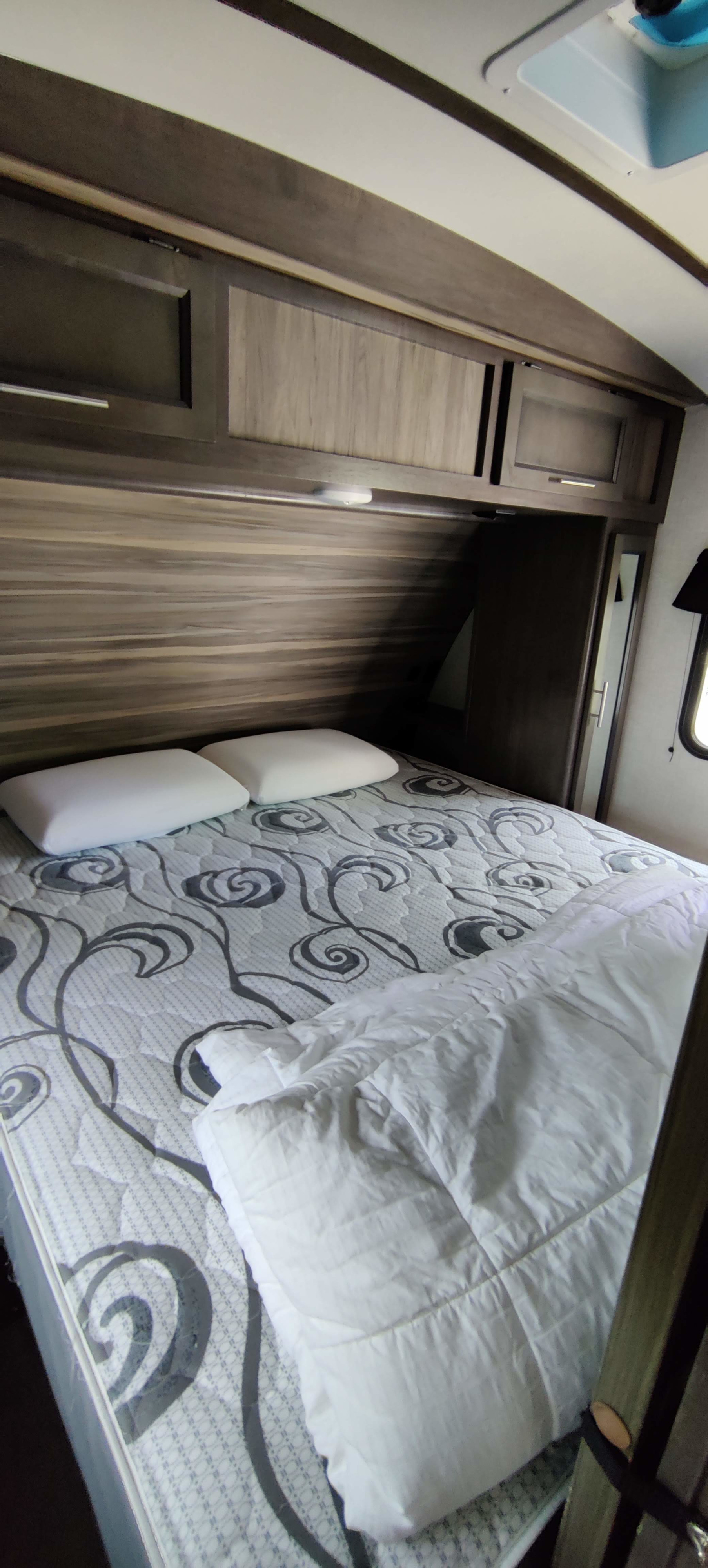 Cozy RV rental bedroom with patterned mattress, white comforter, two pillows, and overhead storage cabinets.. Crossroads RV Sunset Trail Super Lite 2021