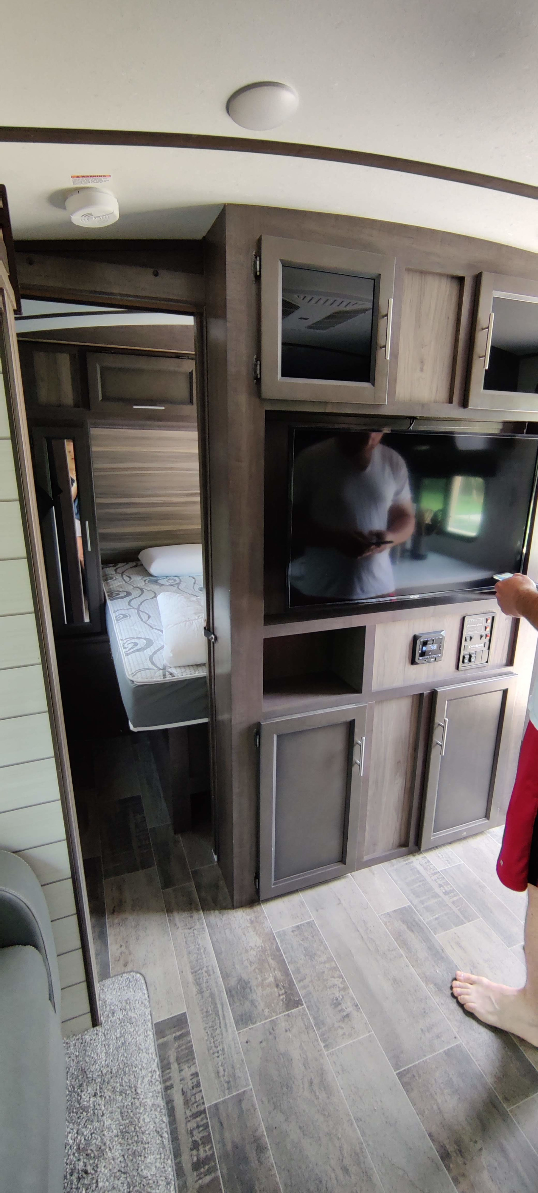 Modern RV rental interior, showing entertainment center, control panels, wood-look floor, and a view into the bedroom.. Crossroads RV Sunset Trail Super Lite 2021
