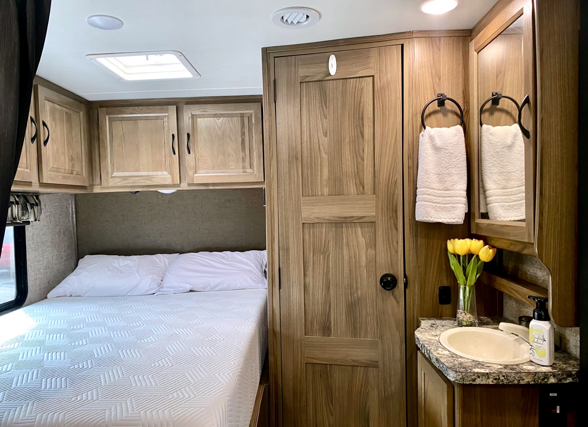 This RV rental features a cozy bedroom with white bedding & wood cabinets, plus a compact bathroom with sink & mirror.. Forest River Coachmen Prism 2018