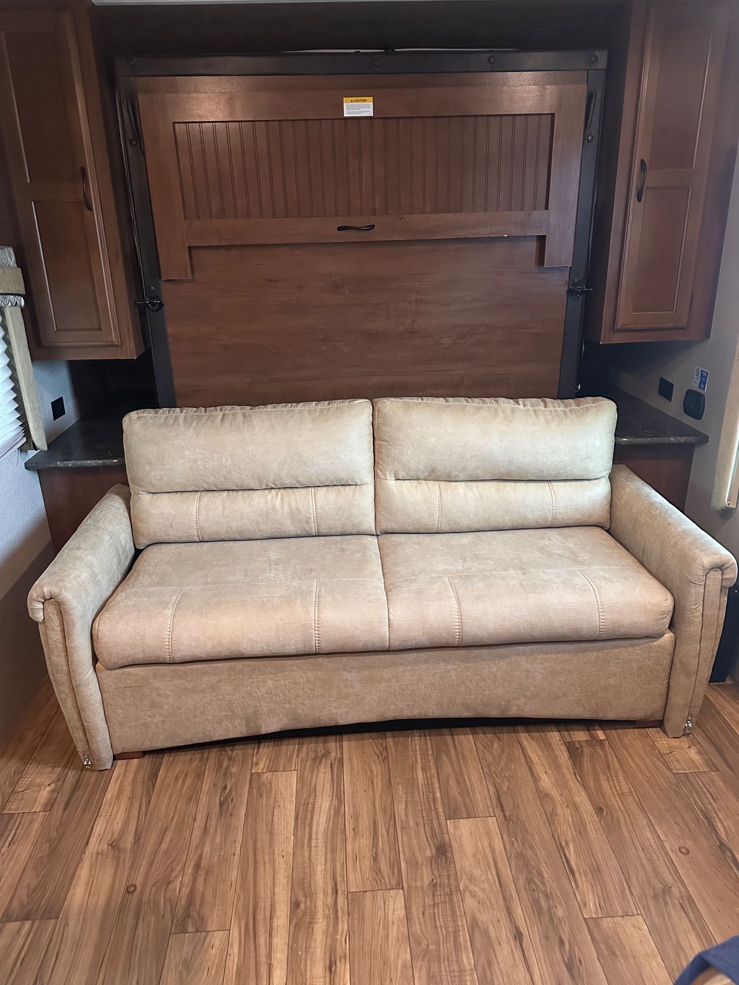 **RV rental:** View of the living area with a tan sofa and an integrated wooden murphy bed folded against the wall.. Jayco Jay Flight 2016