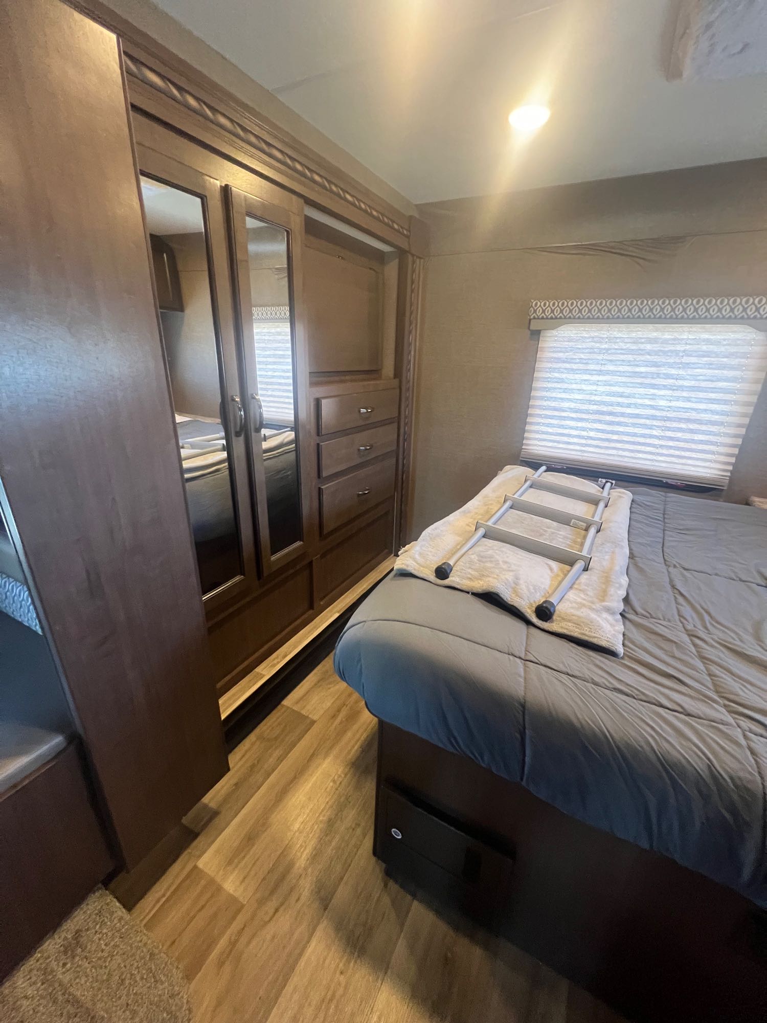 Cozy RV rental bedroom with a comfortable bed, mirrored wardrobe, dresser, and wood-look flooring. Ready for travel!. Thor Freedom Elite 2017