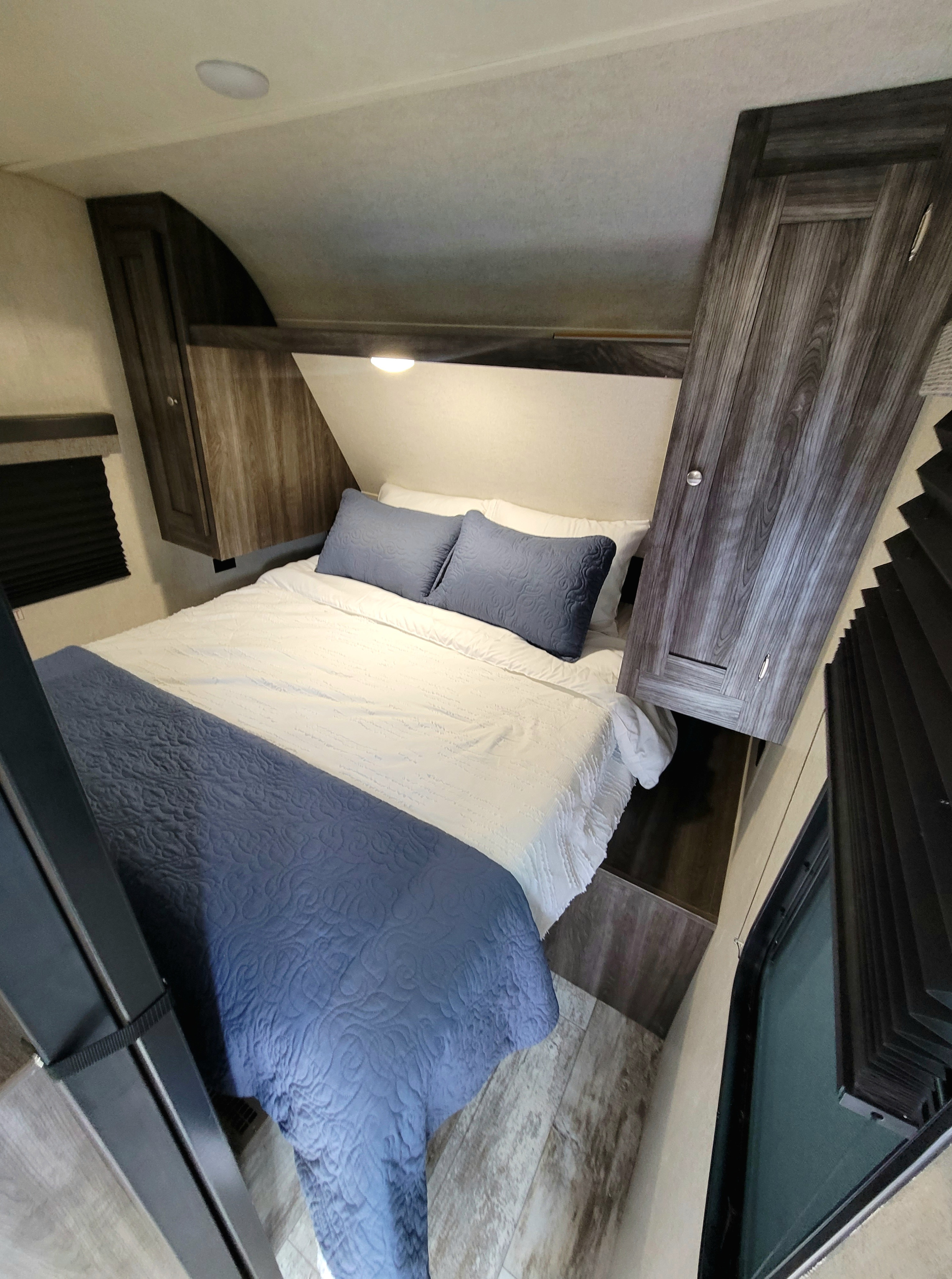 Cozy RV rental bedroom with blue and white bedding, overhead cabinets, and a reading light, perfect for travelers.. Highland Ridge RV Open Range Conventional OT26BHS 2019
