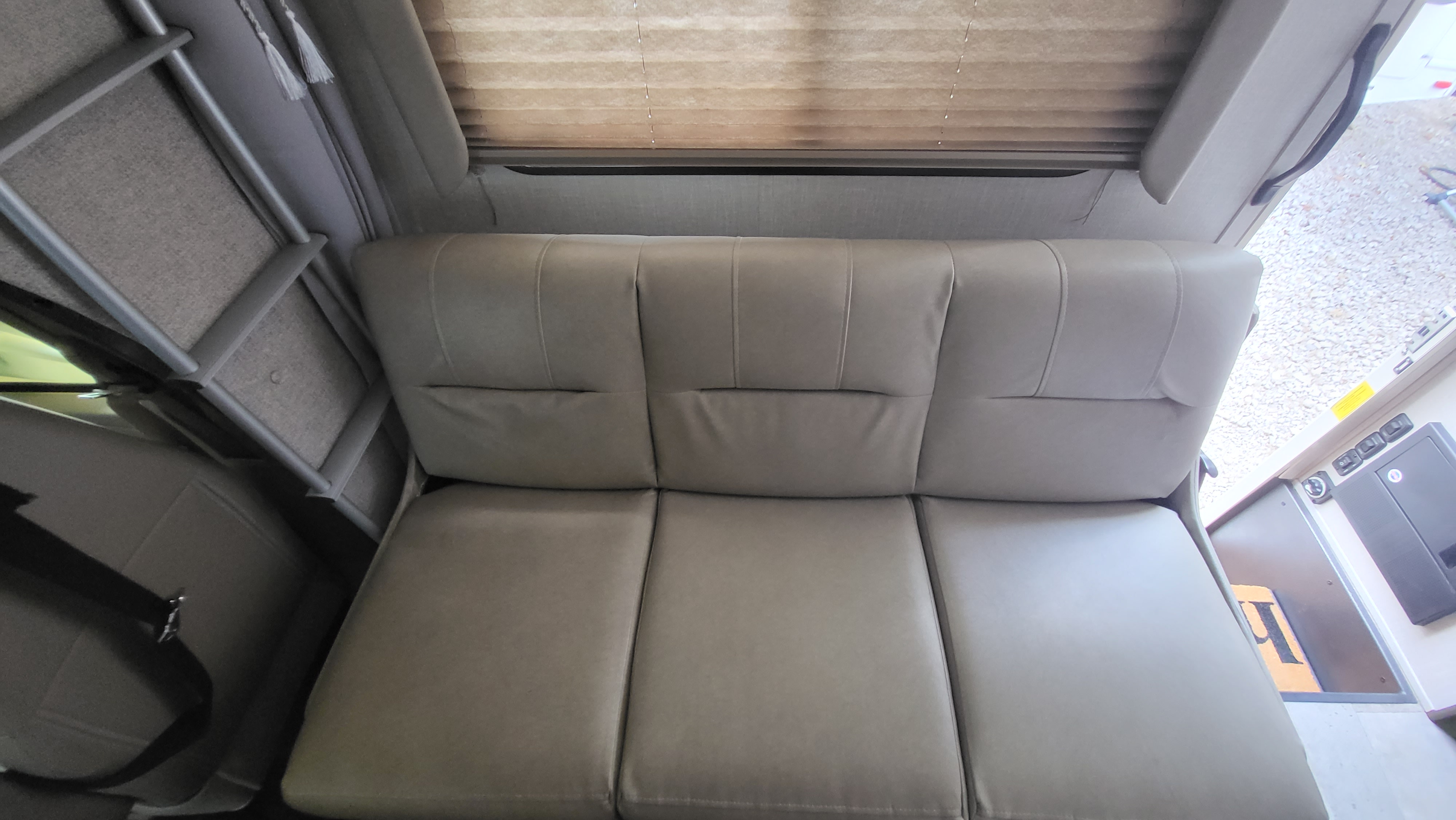 RV rental interior featuring a convertible light gray sofa, overhead bunk ladder, and window with blinds.. Coachmen Freelander 2020