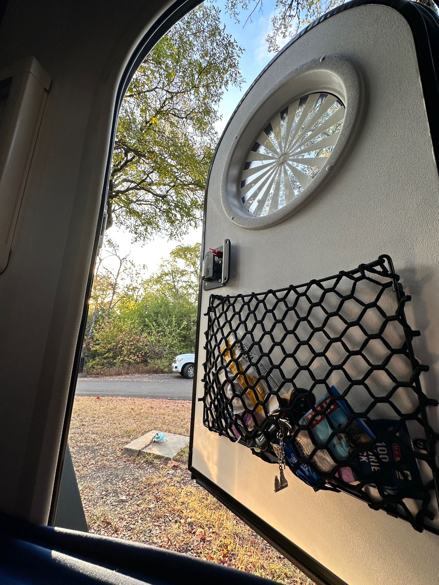 Enjoying nature from an RV rental. Open camper door reveals storage net with snacks, keys, and a serene outdoor scene.. nuCamp T@G 2023