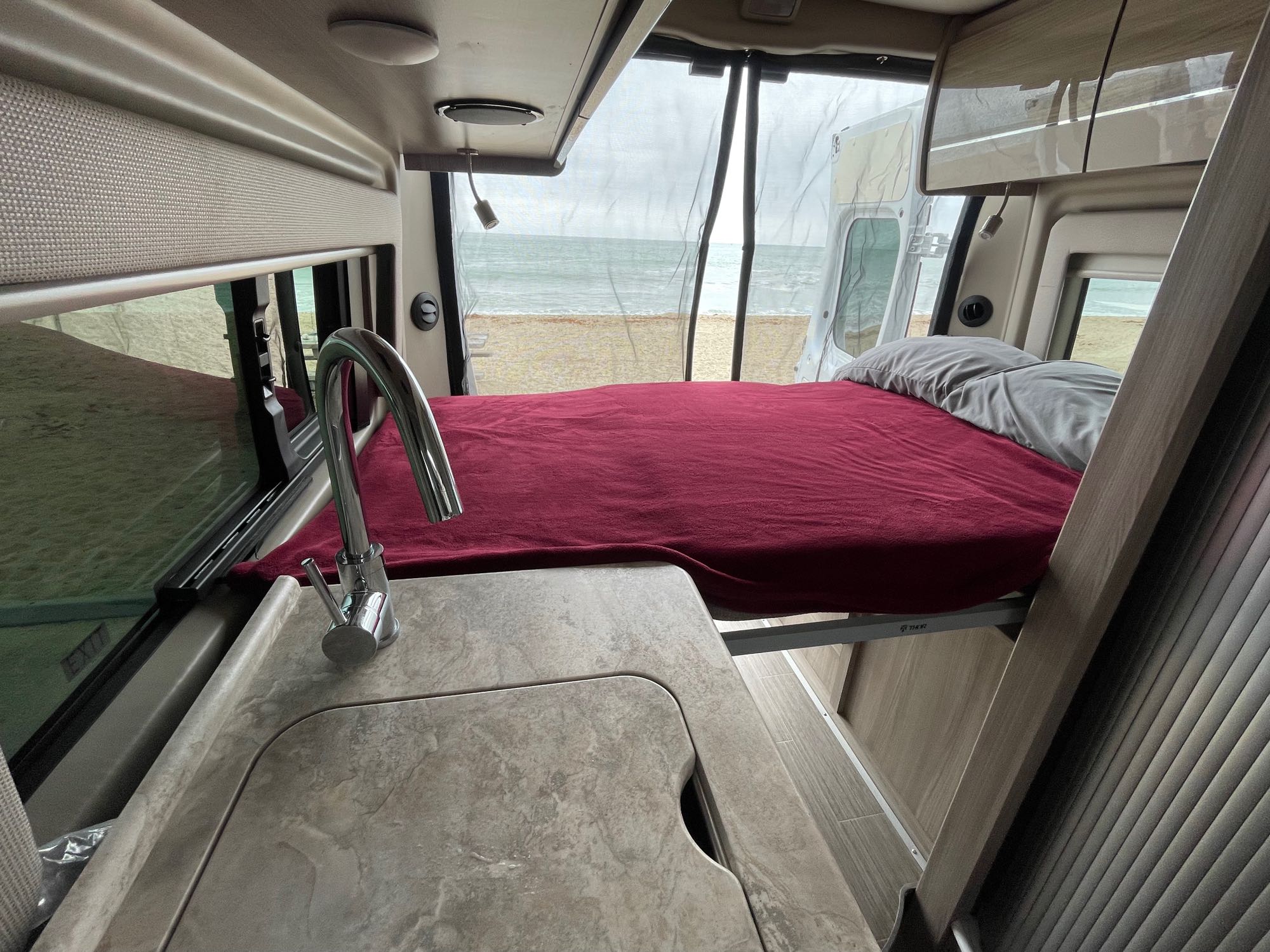 Enjoy this RV rental! Inside, a comfy bed and sink face large windows with a stunning beach and ocean view. Relaxing travel.. Thor Scope 2023