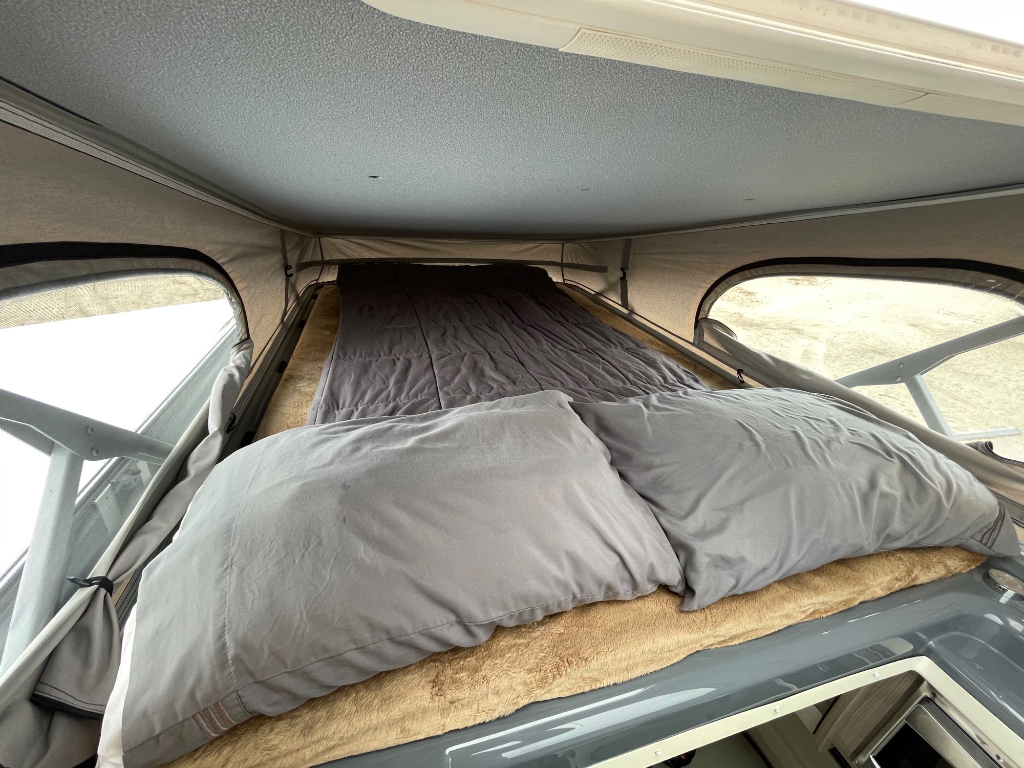 Pop-top bed in an RV rental camper van. A cozy elevated sleeping area with pillows and bedding, ideal for travel.. Thor Scope 2023