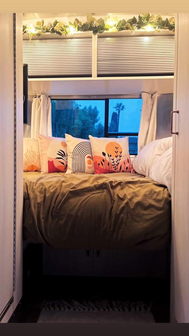 Cozy RV rental bedroom with comfy bed, artistic pillows, warm lights, and a serene night view for travel.. Airstream Bambi 2021