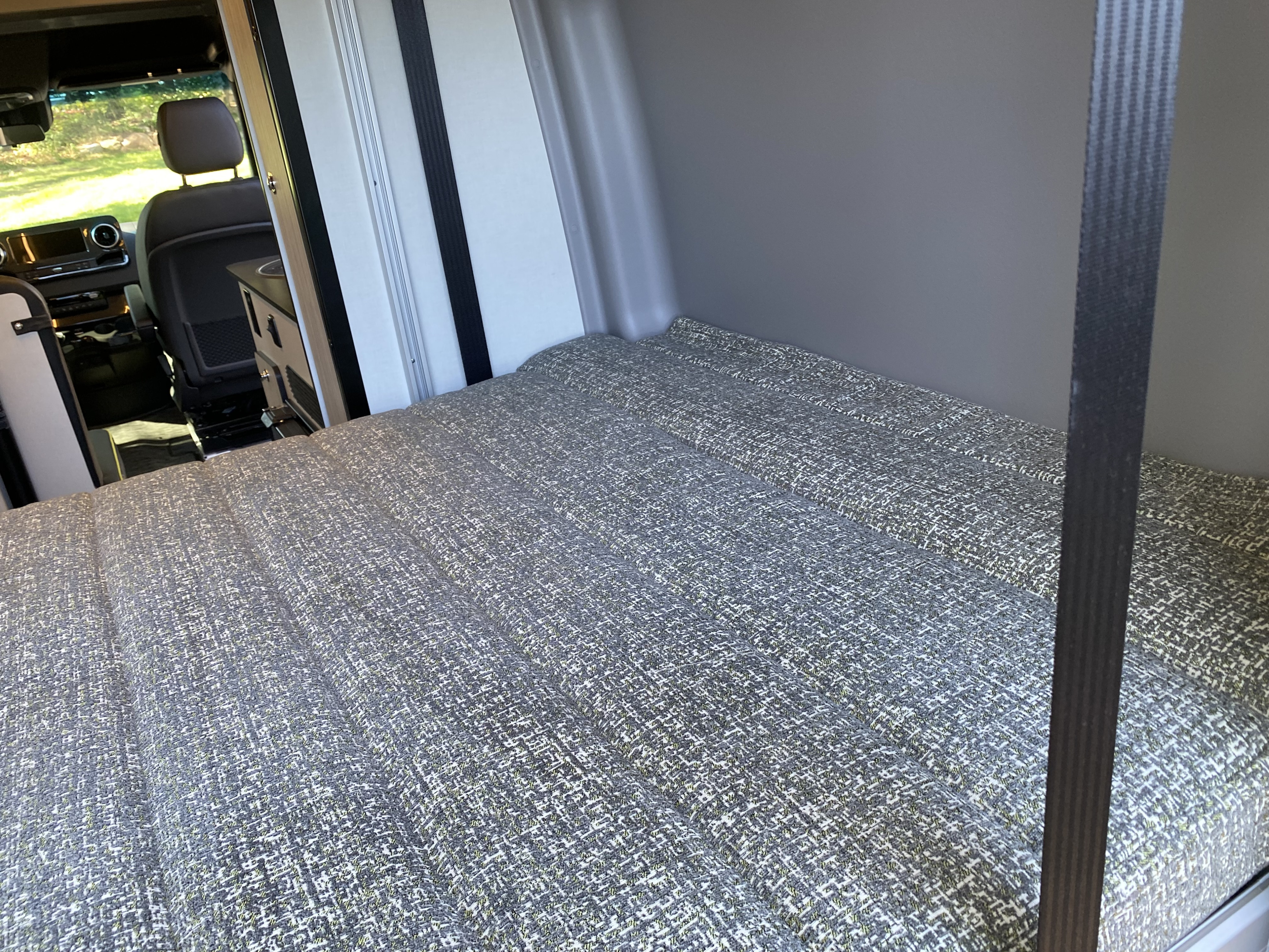 RV rental: Cozy patterned bed inside a camper van, with a glimpse of the front cabin. Perfect for travel comfort.. Winnebago Revel 2020