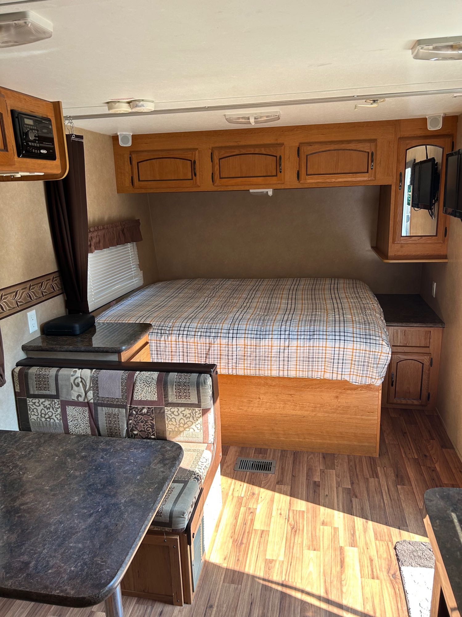 Inside this rv rental: a cozy bedroom with plaid bedding, overhead cabinets, and a dining nook with patterned bench seating.. Forest River Salem 2012