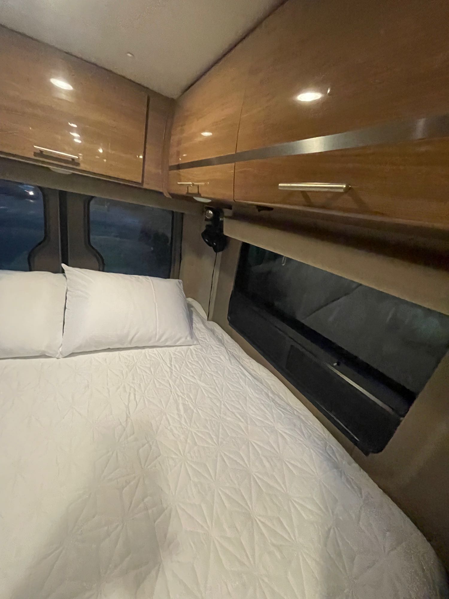 View of a neat RV rental sleeping area: crisp white bedding, pillows, and ample overhead storage.. Winnebago Era 2016