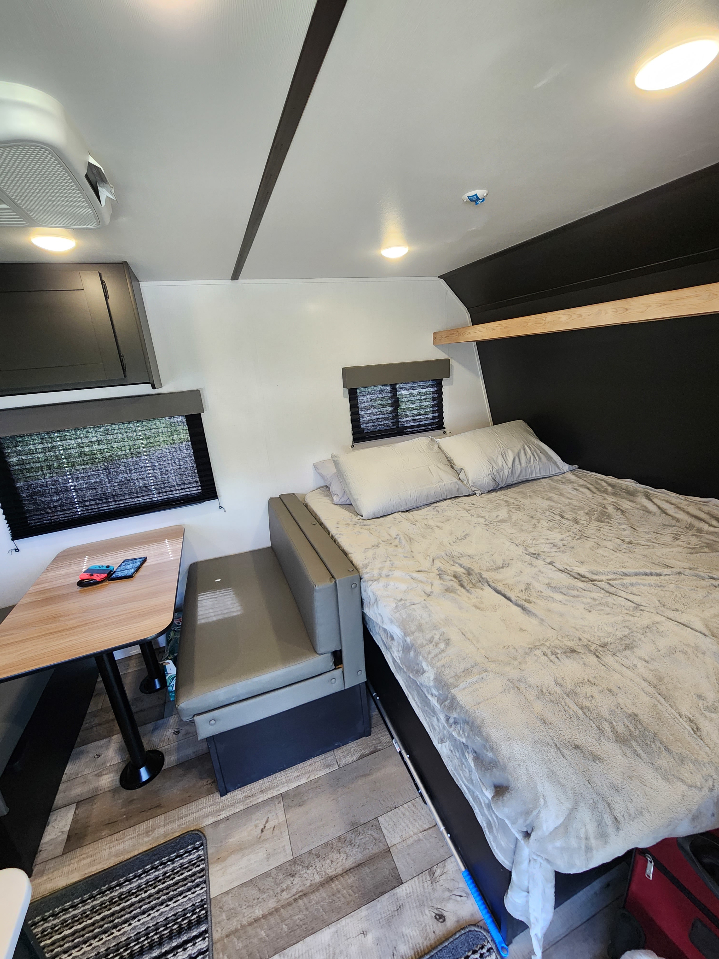 RV rental interior: a comfy bed, dinette with a Nintendo Switch, overhead storage, and windows.. Keystone RV Springdale 2022