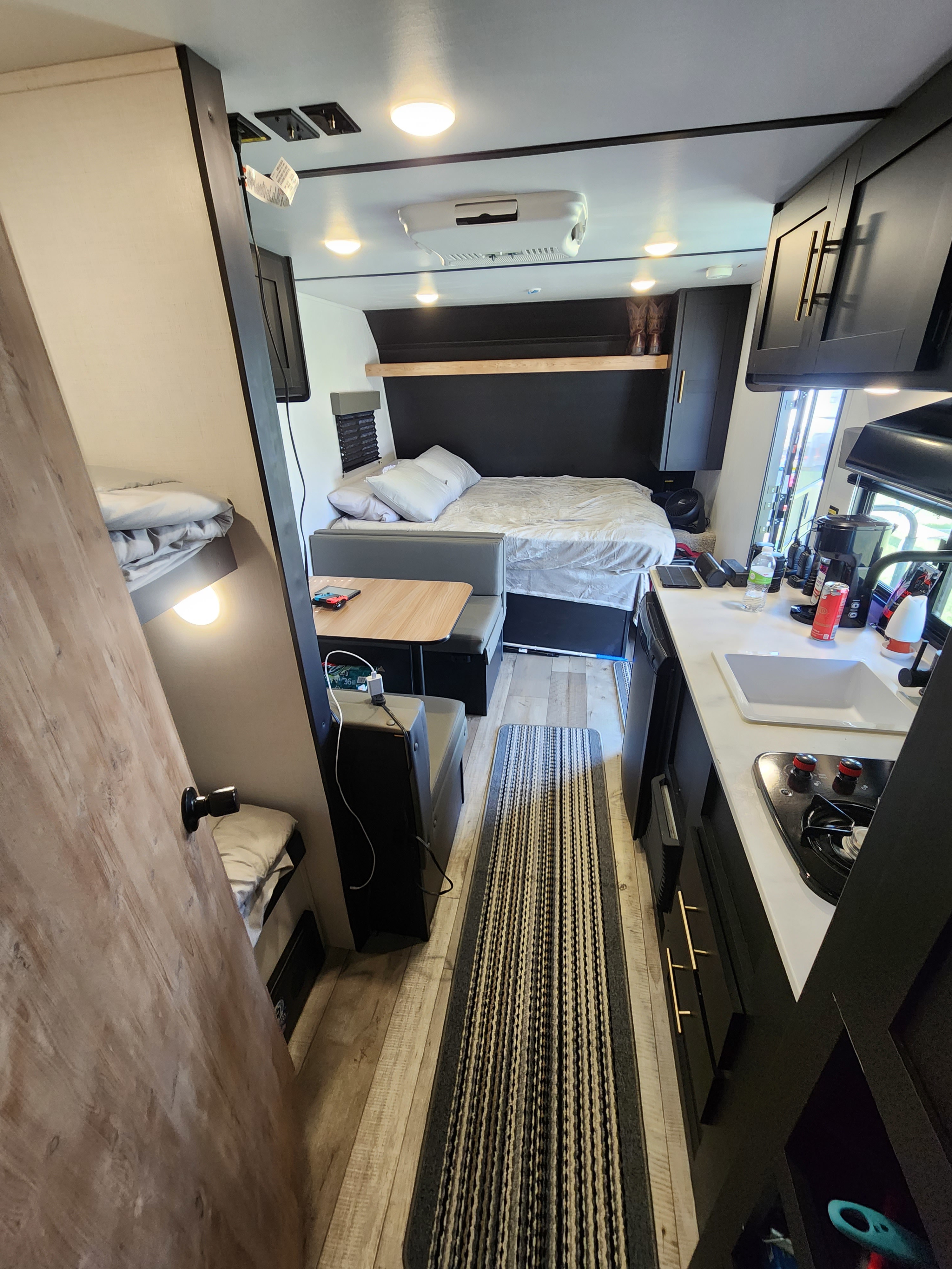 Bright RV rental interior showing bed, dinette, kitchen, and partial bunk. Perfect for compact travel.. Keystone RV Springdale 2022