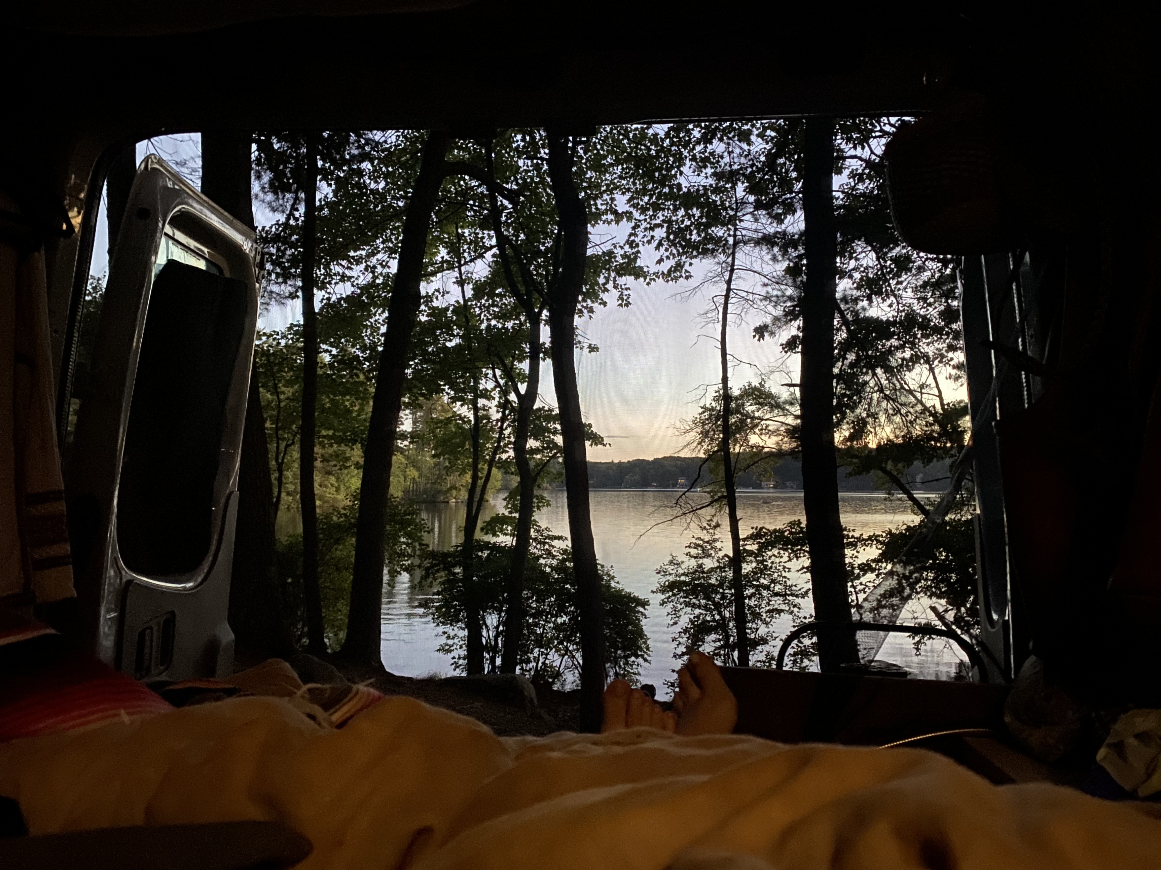 Cozy view from an RV rental, feet up, overlooking a tranquil lake through silhouetted trees at sunset.. Mercedes-Benz Sprinter 2012