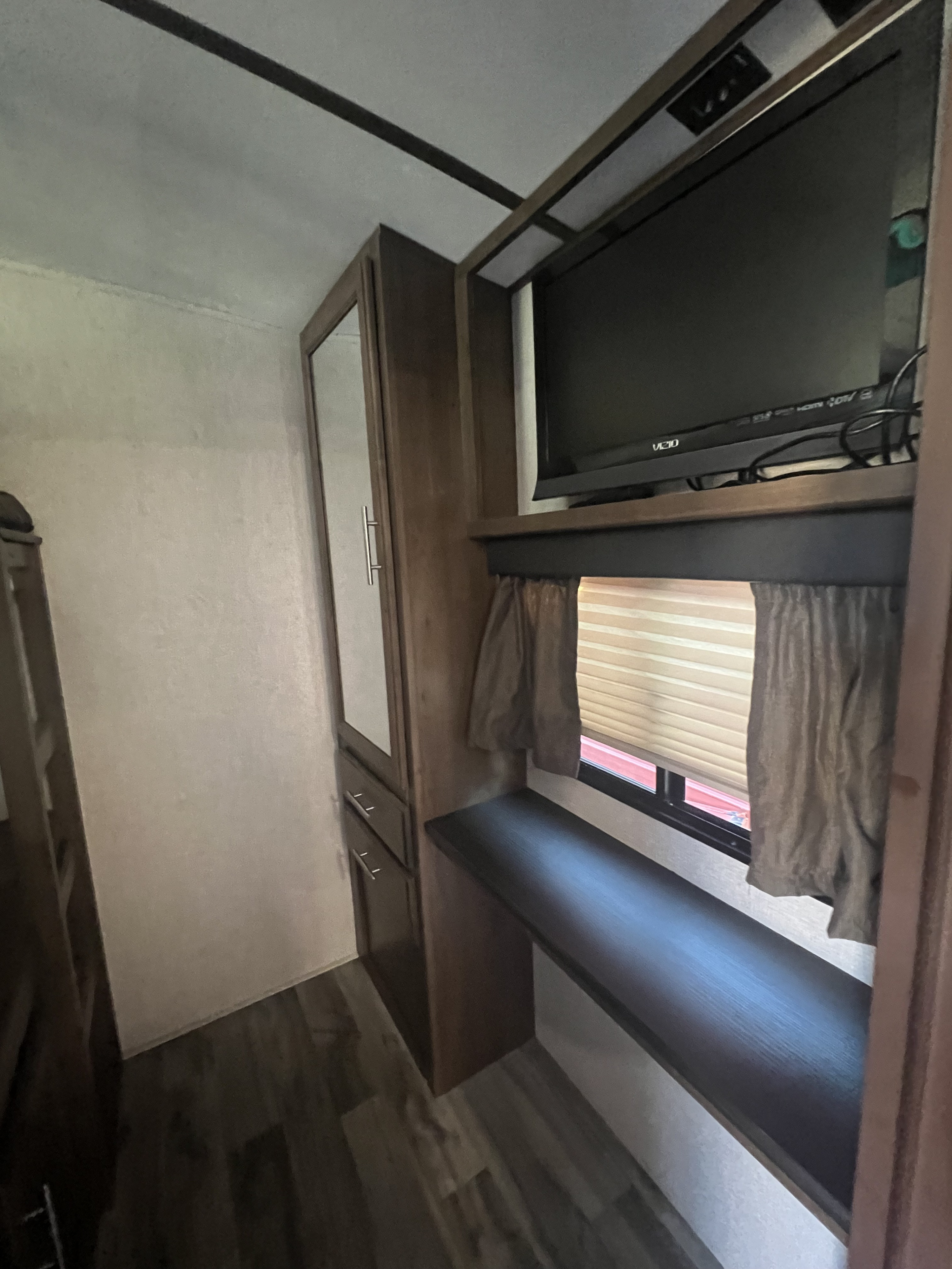Inside an RV rental: Features a mounted TV, built-in shelf/desk, window with blinds, and mirrored storage cabinet.. Keystone RV Cougar 2019