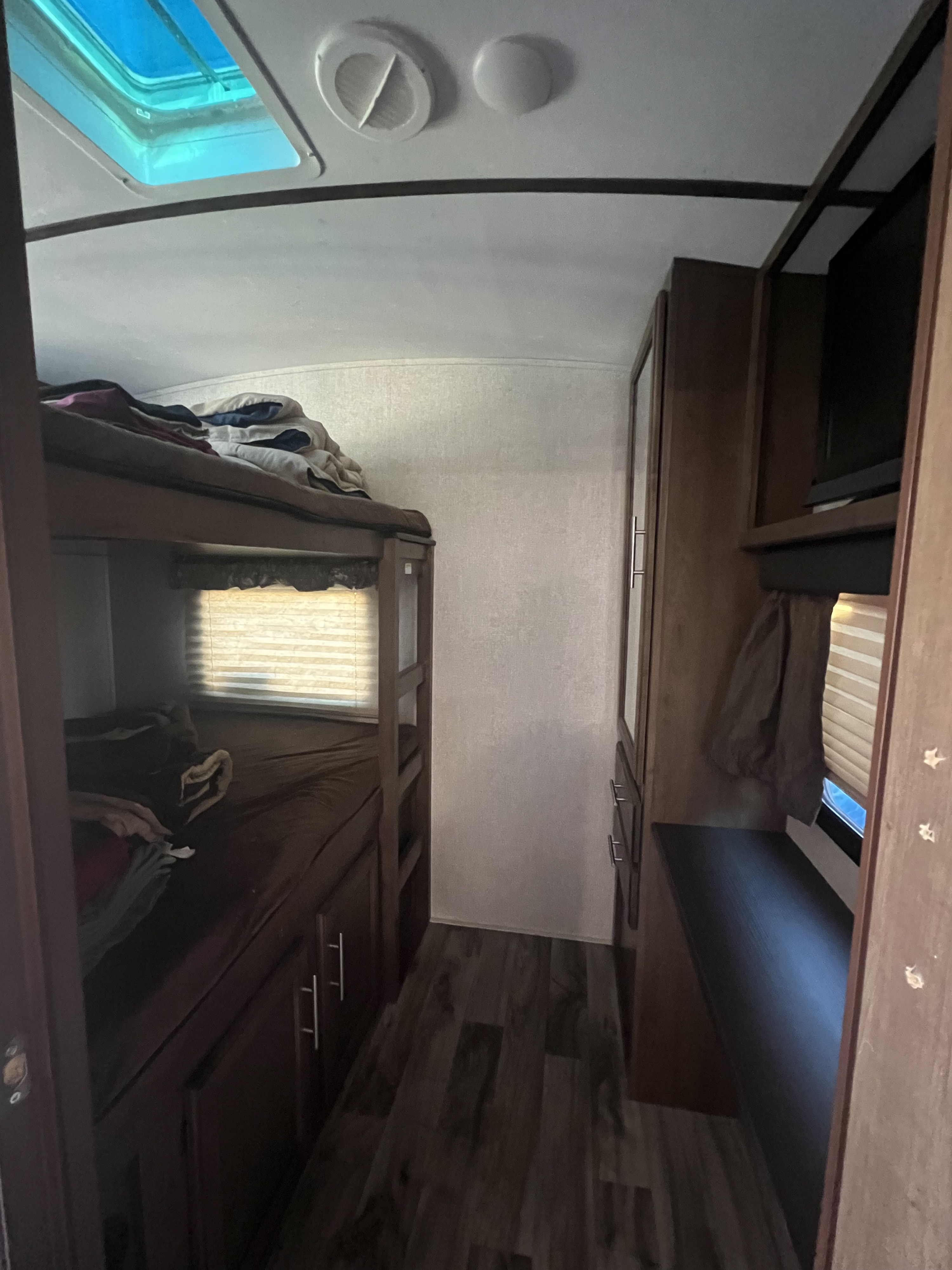 Cozy RV rental interior with dark wood bunk beds and storage cabinetry along a narrow hallway. A skylight brightens the ceiling.. Keystone RV Cougar 2019